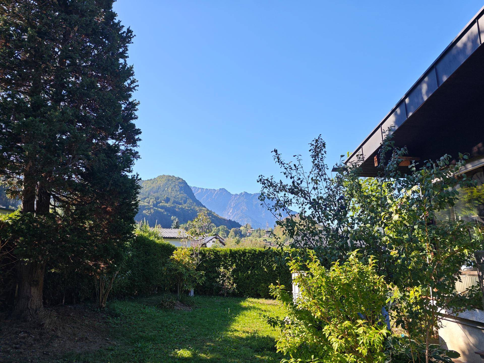 Gepflegter Garten mit Rasenfläche und Bäumen, der einen weiten Blick auf die umliegenden Berge bietet.