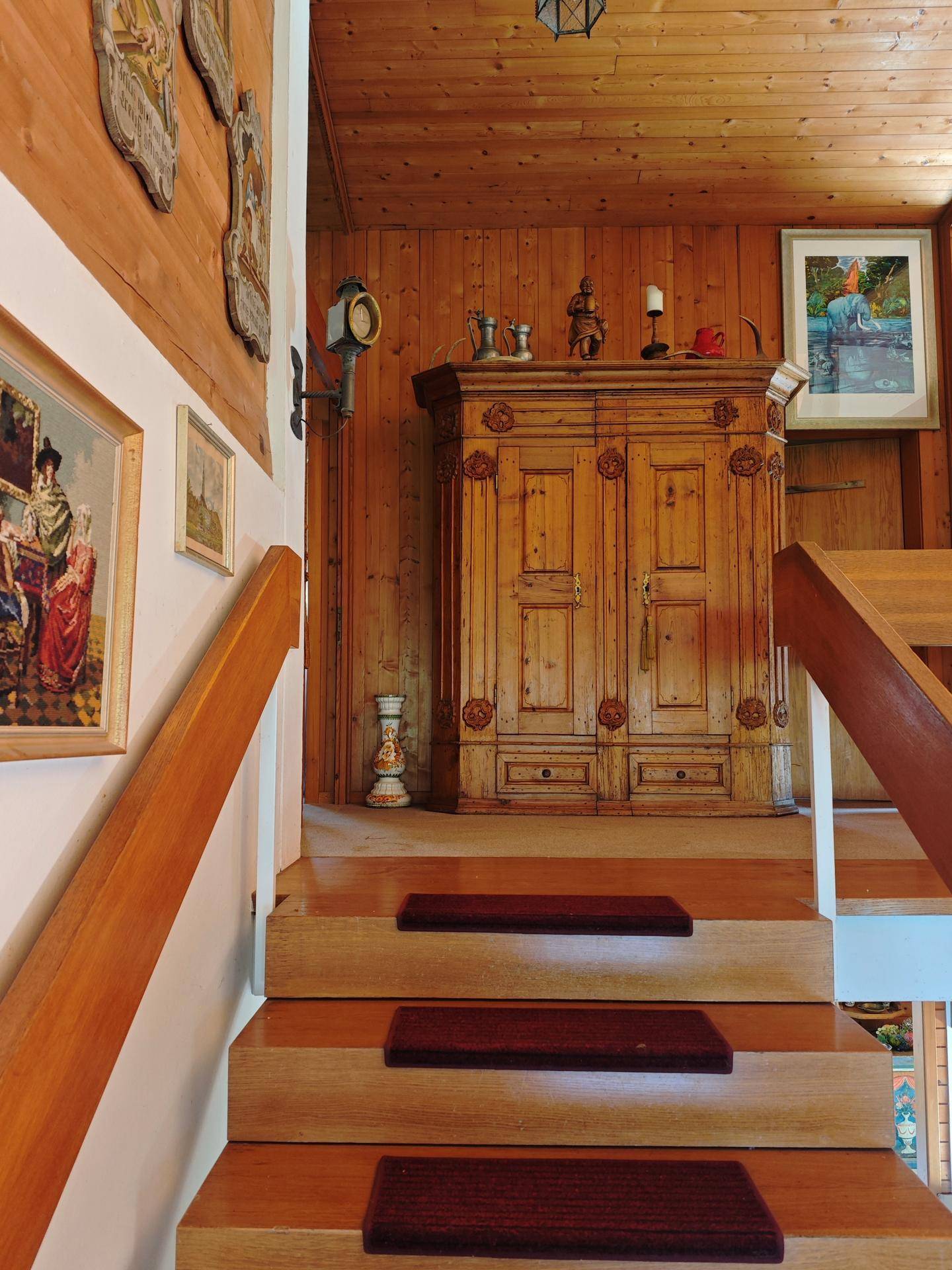 Rustikaler Treppenaufgang mit Holzvertäfelung und einem antiken Holzschrank, der den traditionellen Stil unterstreicht.
