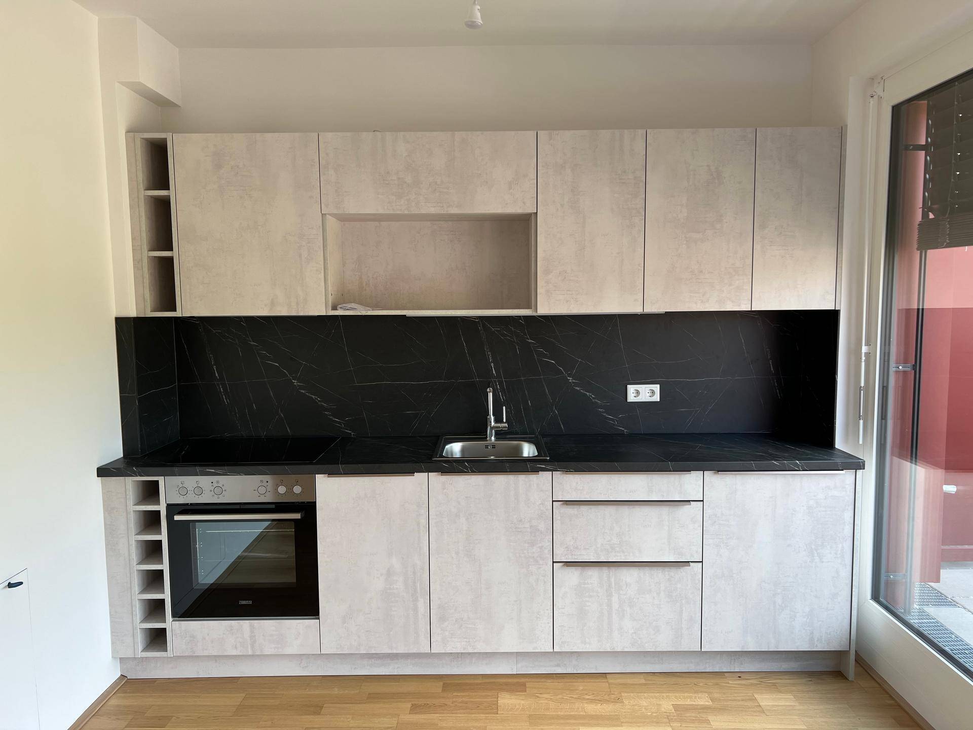 Neue Einbauküche mit hellen Fronten, dunkler Arbeitsplatte und integriertem Backofen.
