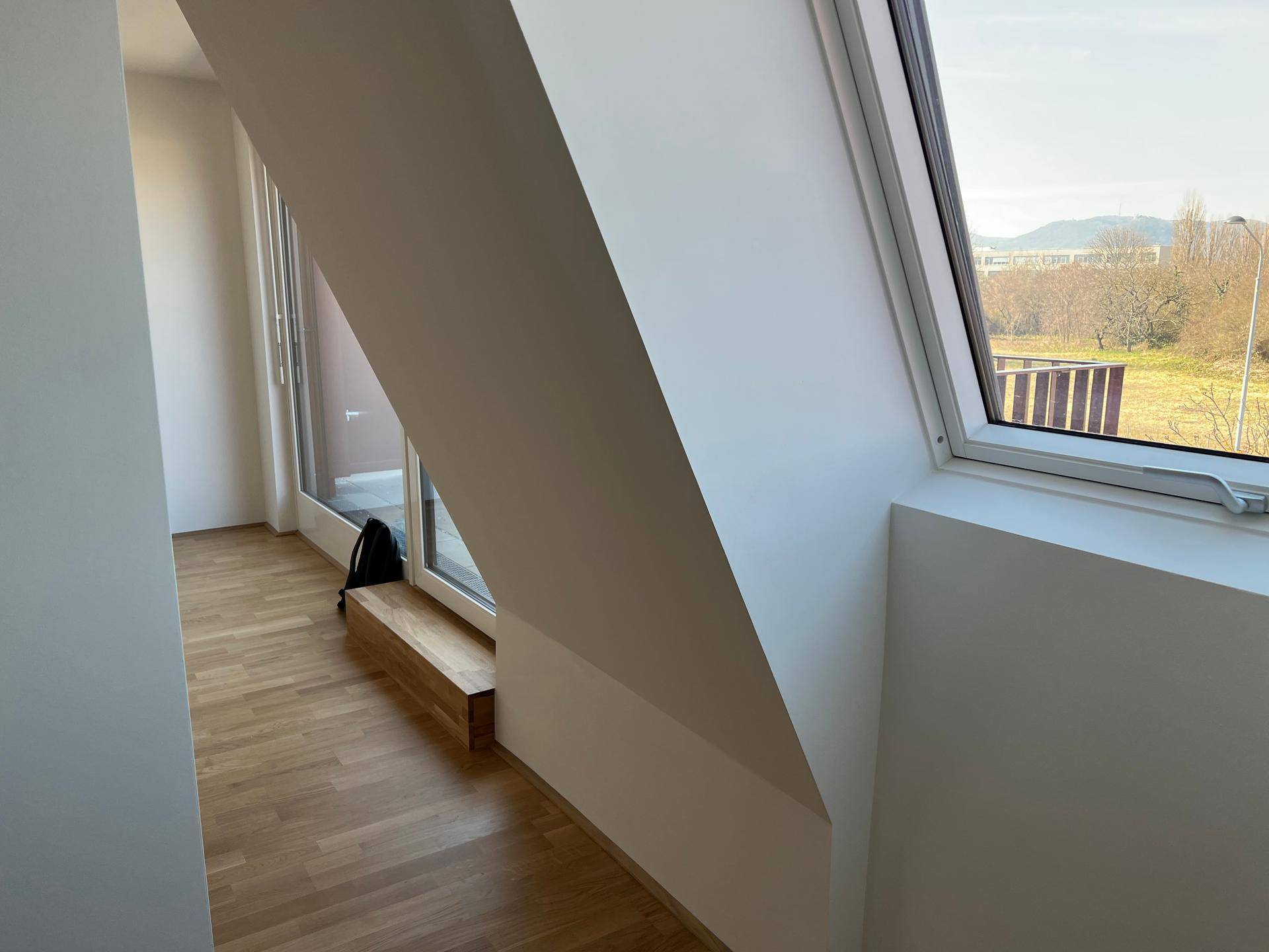 Heller Raum im Dachgeschoss mit schräger Decke, Holzboden und Blick ins Grüne.