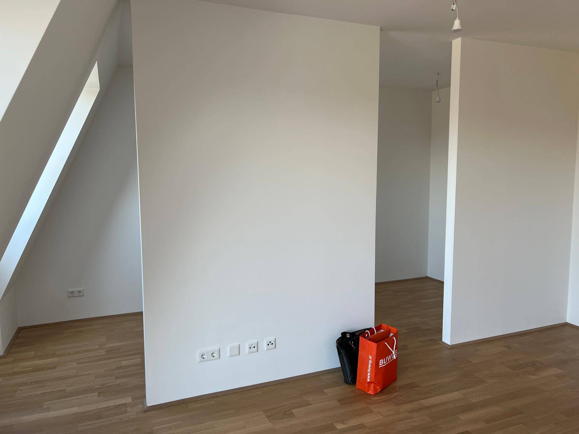 Leerer Raum im Dachgeschoss mit schrägen Wänden, Holzboden und viel Tageslicht.