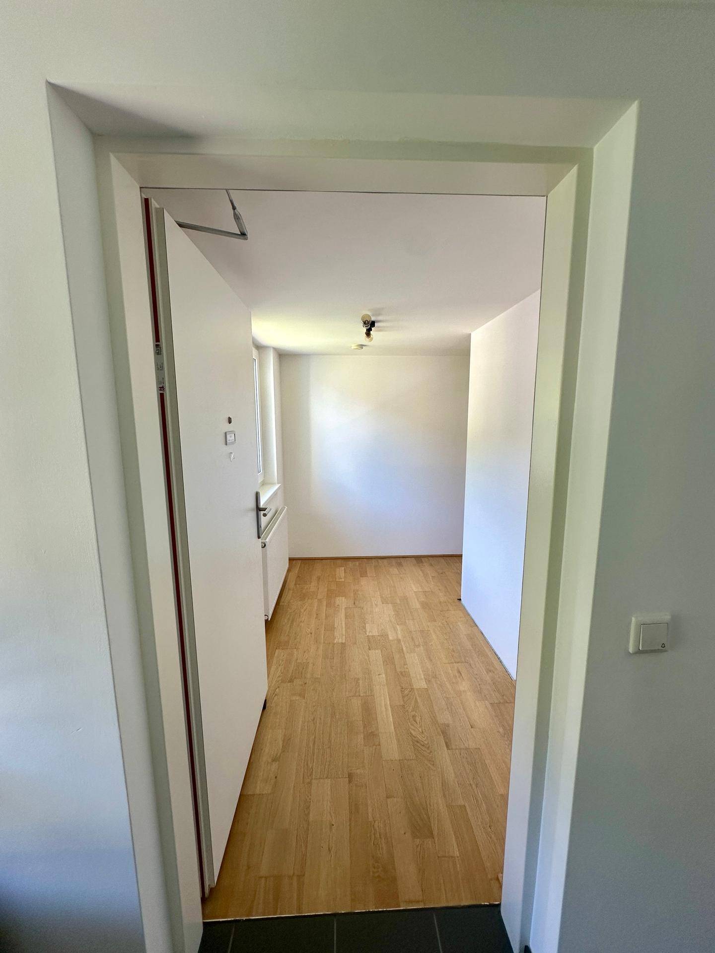 Blick durch eine Tür in einen hellen Flur mit Holzboden, der zu weiteren Räumen führt.