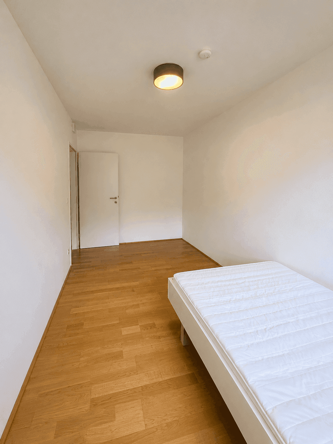 Helles Schlafzimmer mit Holzboden und einfacher Einrichtung, ideal als Gäste- oder Kinderzimmer.