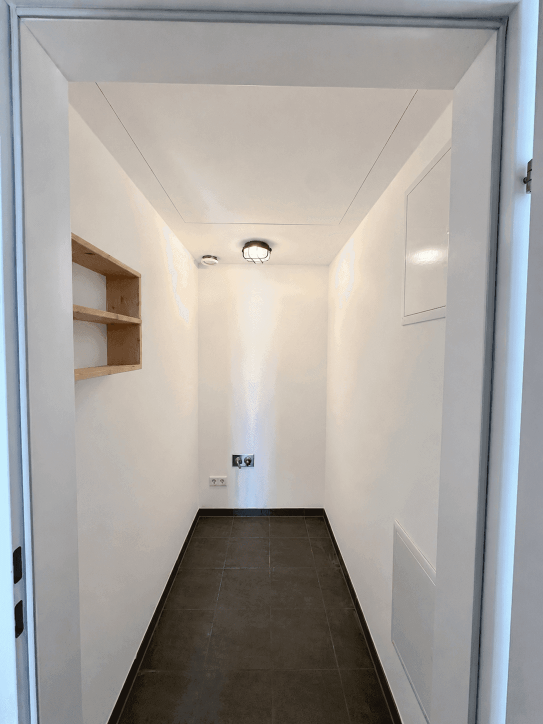 Praktischer Abstellraum mit Fliesenboden, Regalen und Anschlüssen für Waschmaschine oder Trockner.