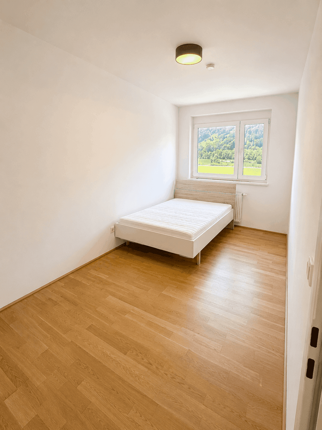Gemütliches Schlafzimmer mit Einzelbett, Holzboden und Fenster mit Blick ins Grüne.
