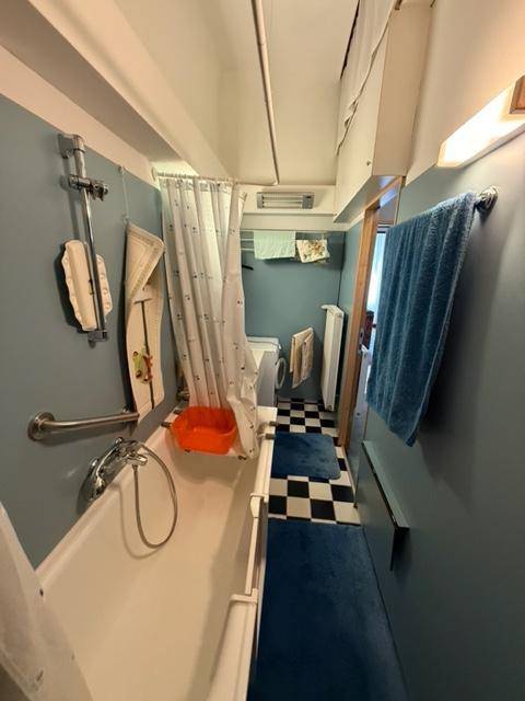 Langes Badezimmer mit Badewanne, Duschvorhang und einem schwarz-weiß karierten Boden.