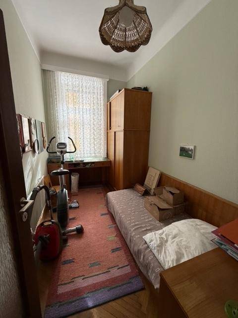 Kleines Schlafzimmer mit Einzelbett, Trainingsgerät und einem Fenster mit Vorhängen.
