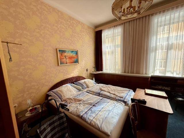 Schlafzimmer mit Doppelbett, Nachttischen und zwei großen Fenstern mit Vorhängen.