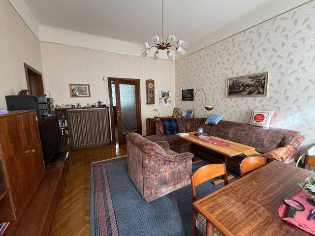 Wohn-Essbereich mit Ecksofa, Esstisch und einem Teppich, der den Holzboden bedeckt.