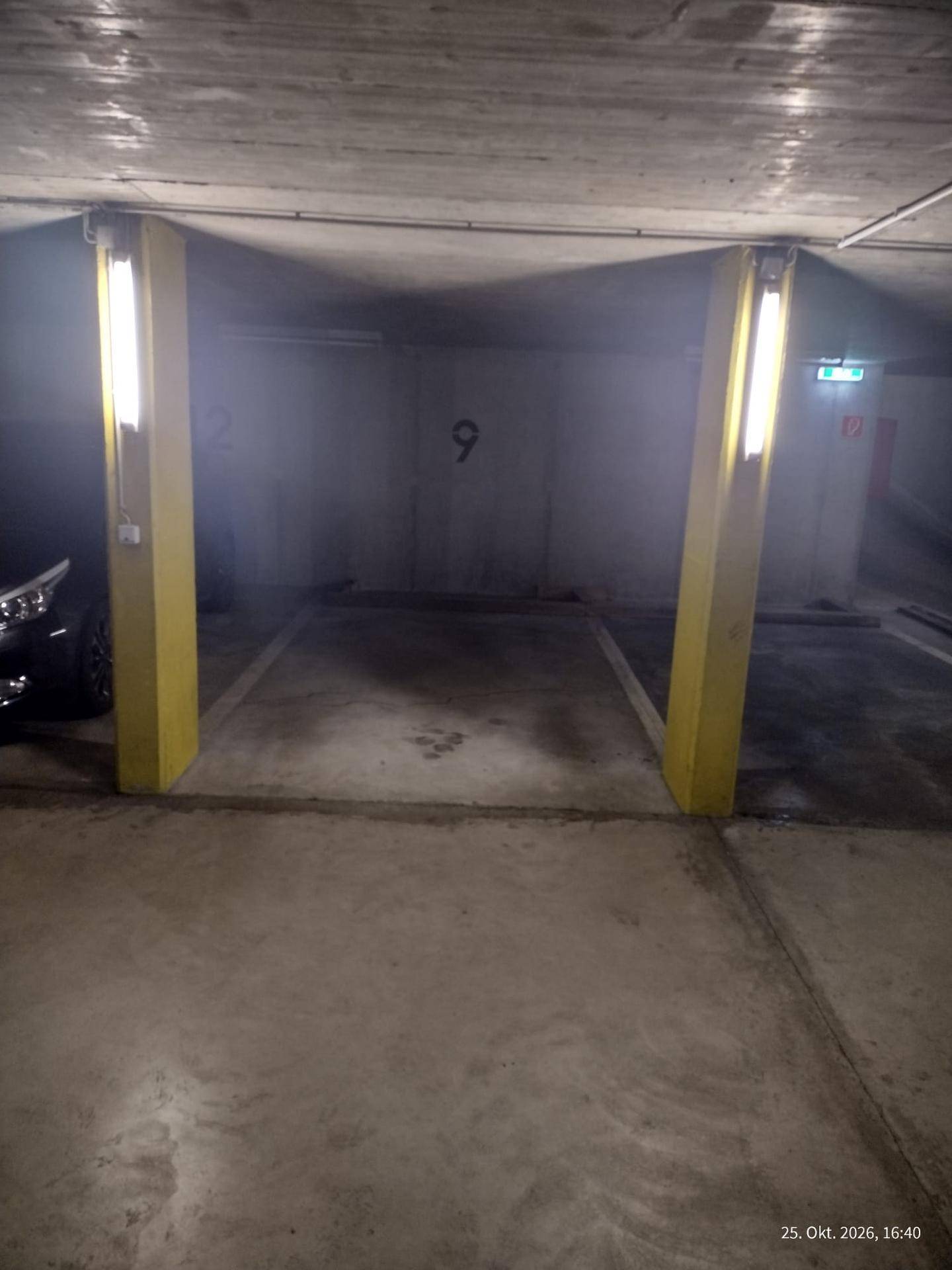 Leerer Parkplatz in der Tiefgarage, begrenzt durch gelbe Säulen und Bodenmarkierungen.