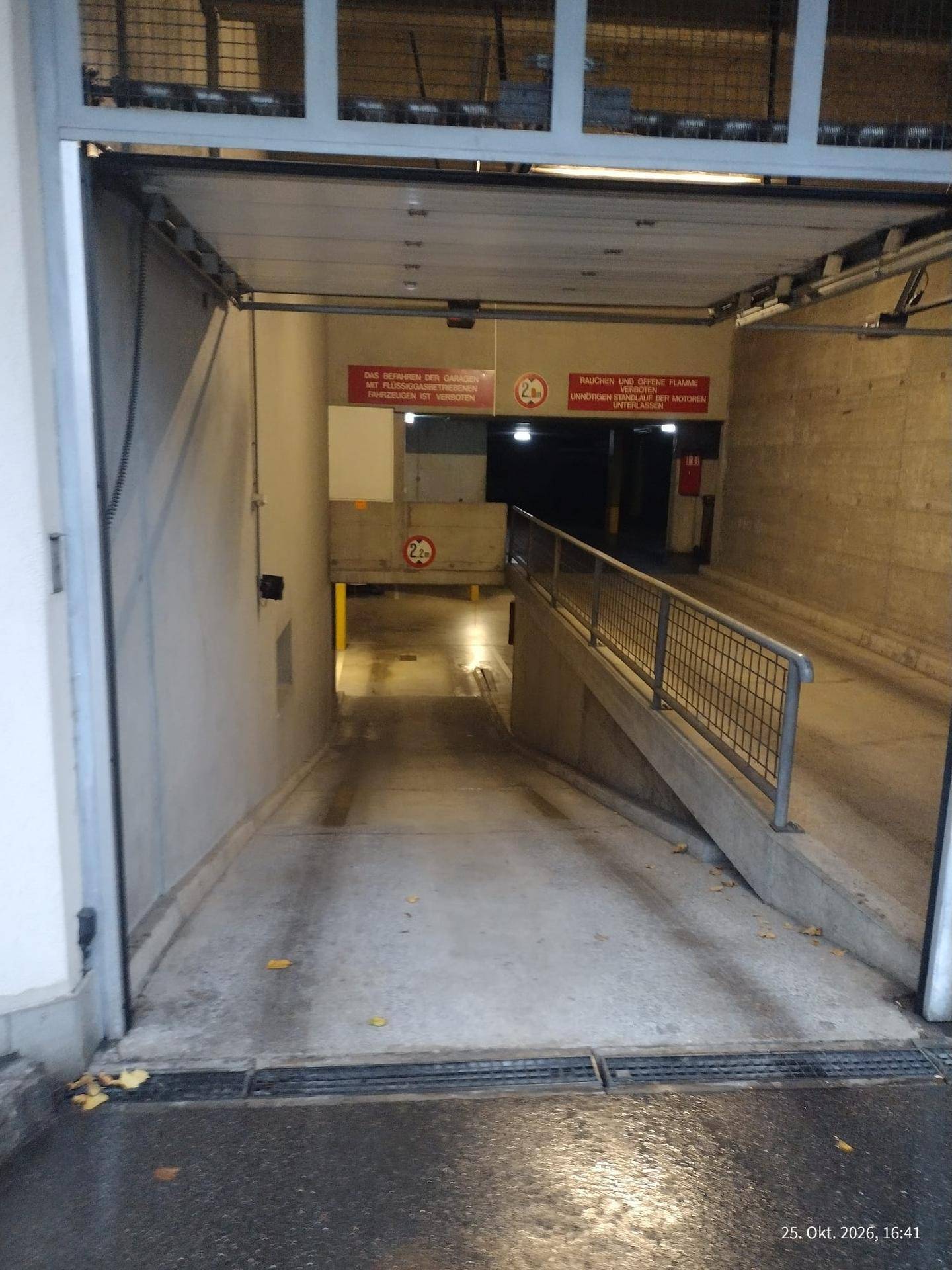 Weitläufige Einfahrt zur Tiefgarage mit Betonrampe und Metallgeländer, gut beleuchtet und zugänglich.