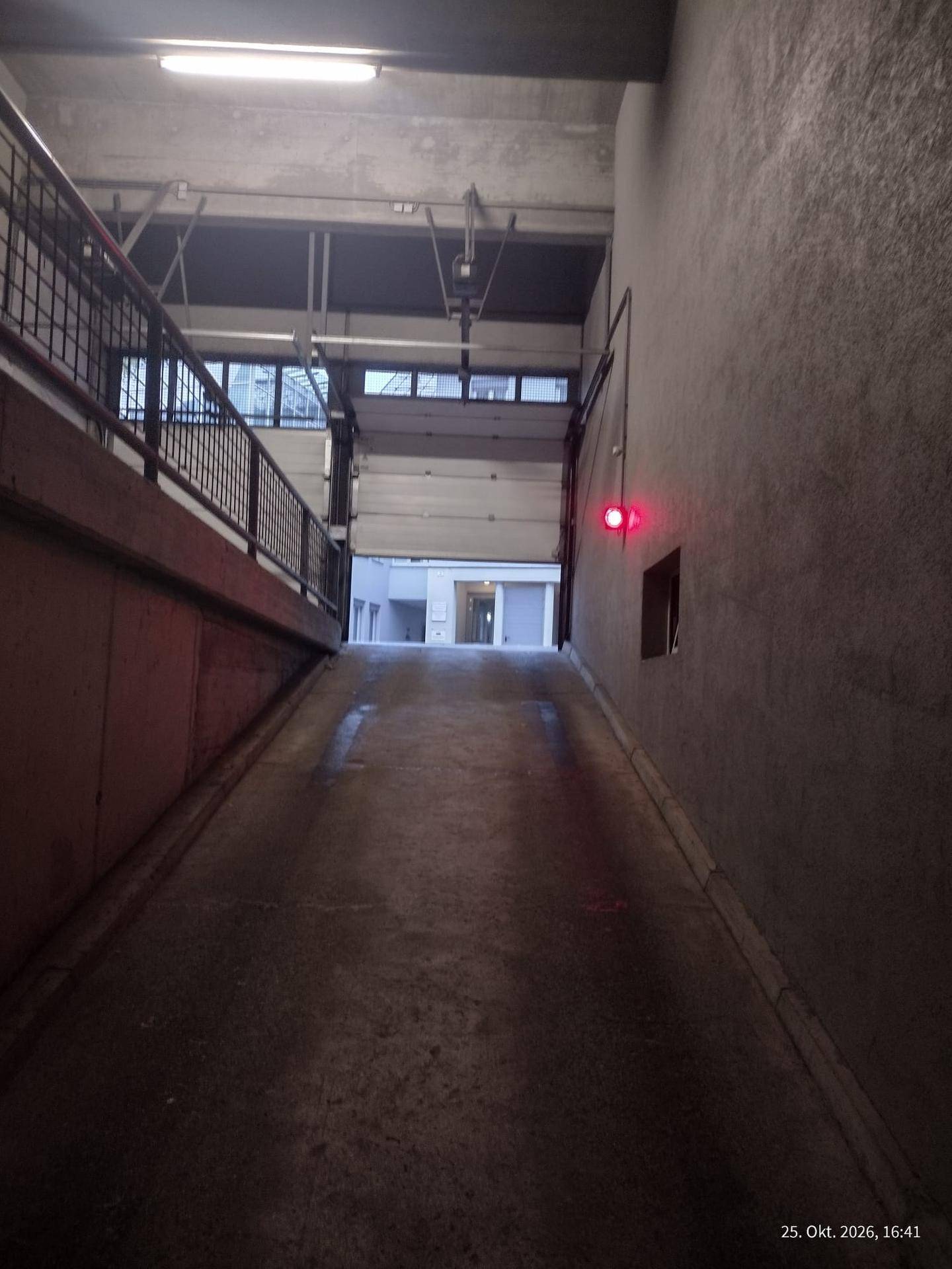 Tiefgaragenrampe mit Betonwänden und Metallgeländer, Blick zum Ausgang mit rotem Signal.