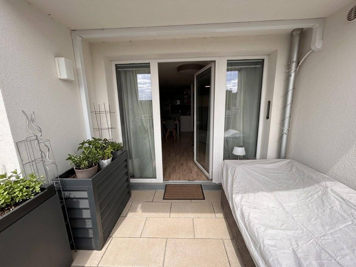 Heller Balkon mit Fliesenboden, Pflanzen und Sitzgelegenheit, zugänglich vom Wohnbereich.