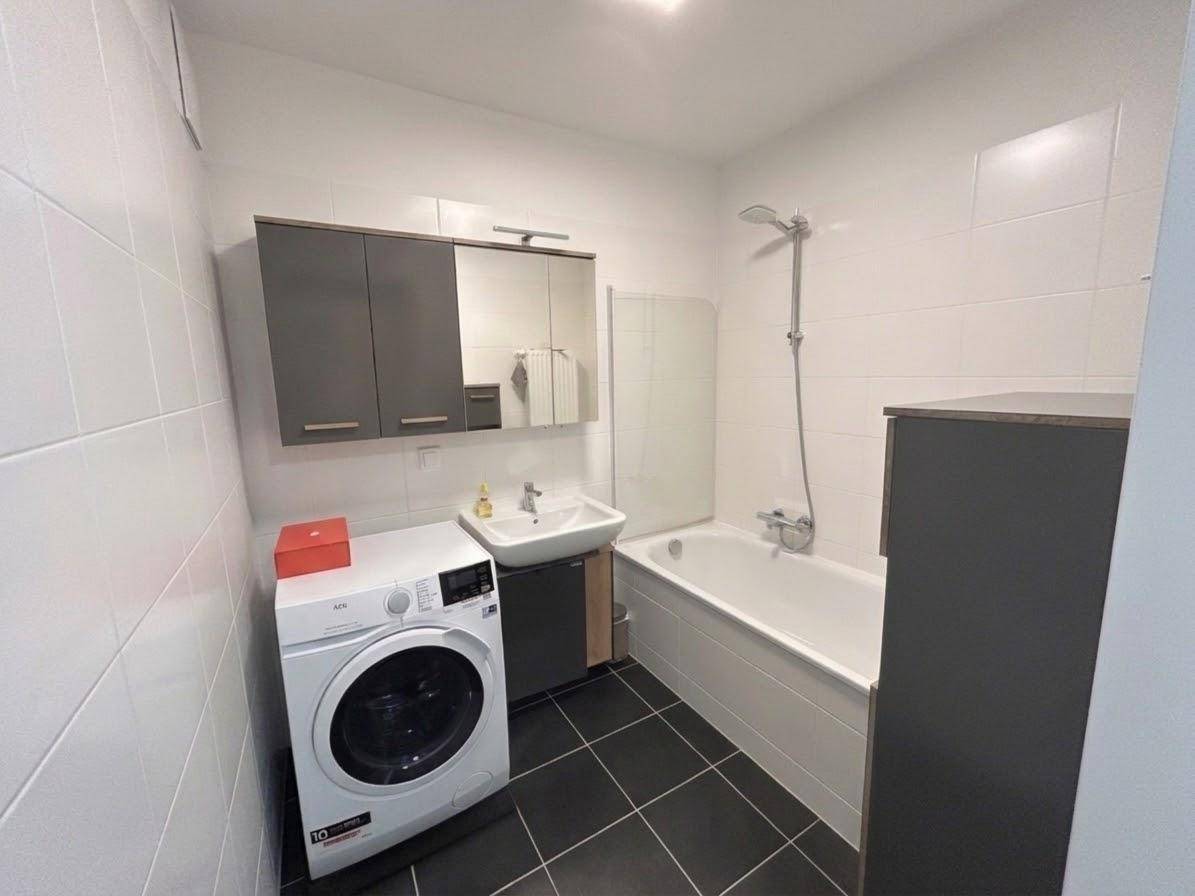 Badezimmer mit Badewanne, Waschmaschine und dunklen Bodenfliesen.