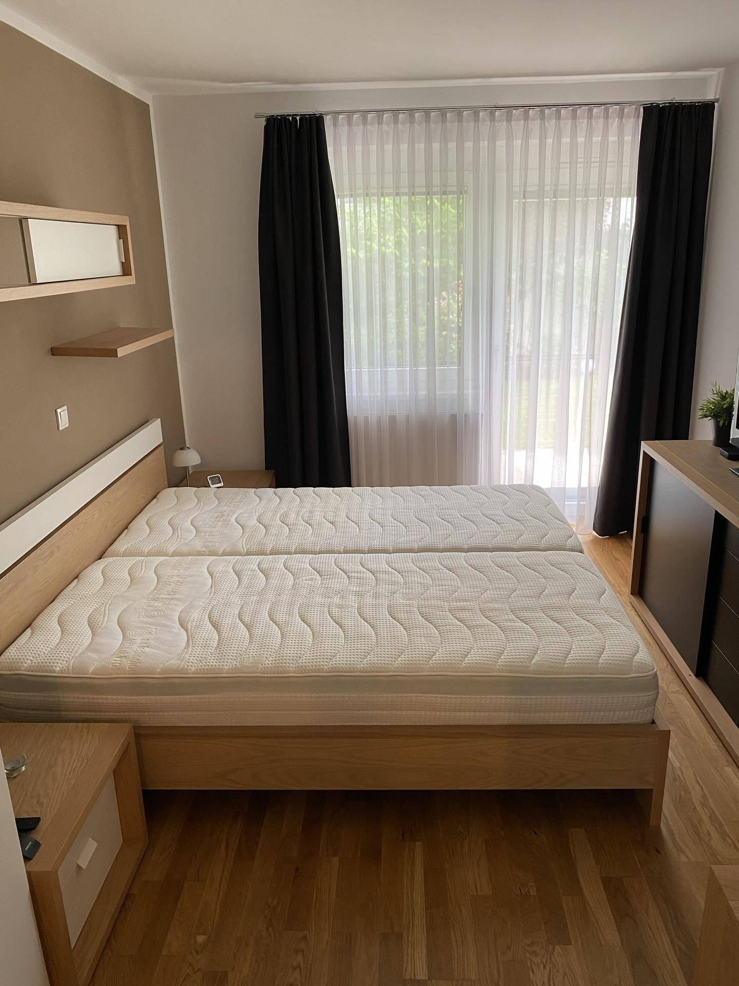 Helles Schlafzimmer mit zwei Einzelbetten, Holzmöbeln und Zugang zum Balkon.