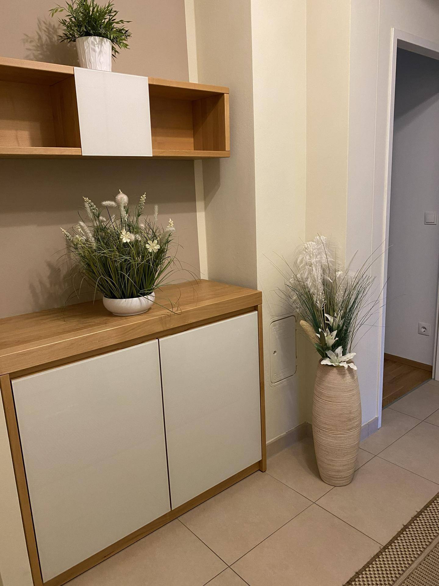 Heller Flur mit Holzmöbeln, dekorativen Pflanzen und Fliesenboden.