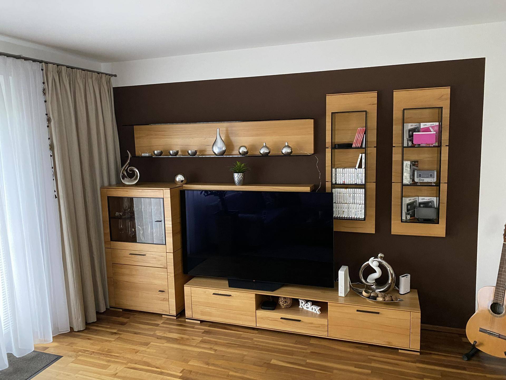 Gemütliches Wohnzimmer mit Holzboden, brauner Akzentwand und moderner TV-Möbelkombination.