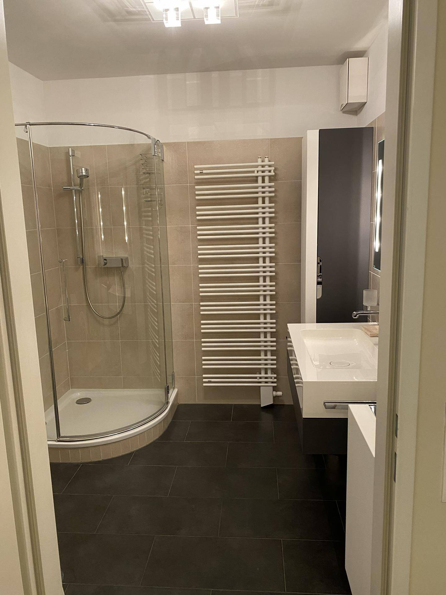 Modernes Badezimmer mit Duschkabine, Handtuchheizkörper und stilvollem Waschtisch.