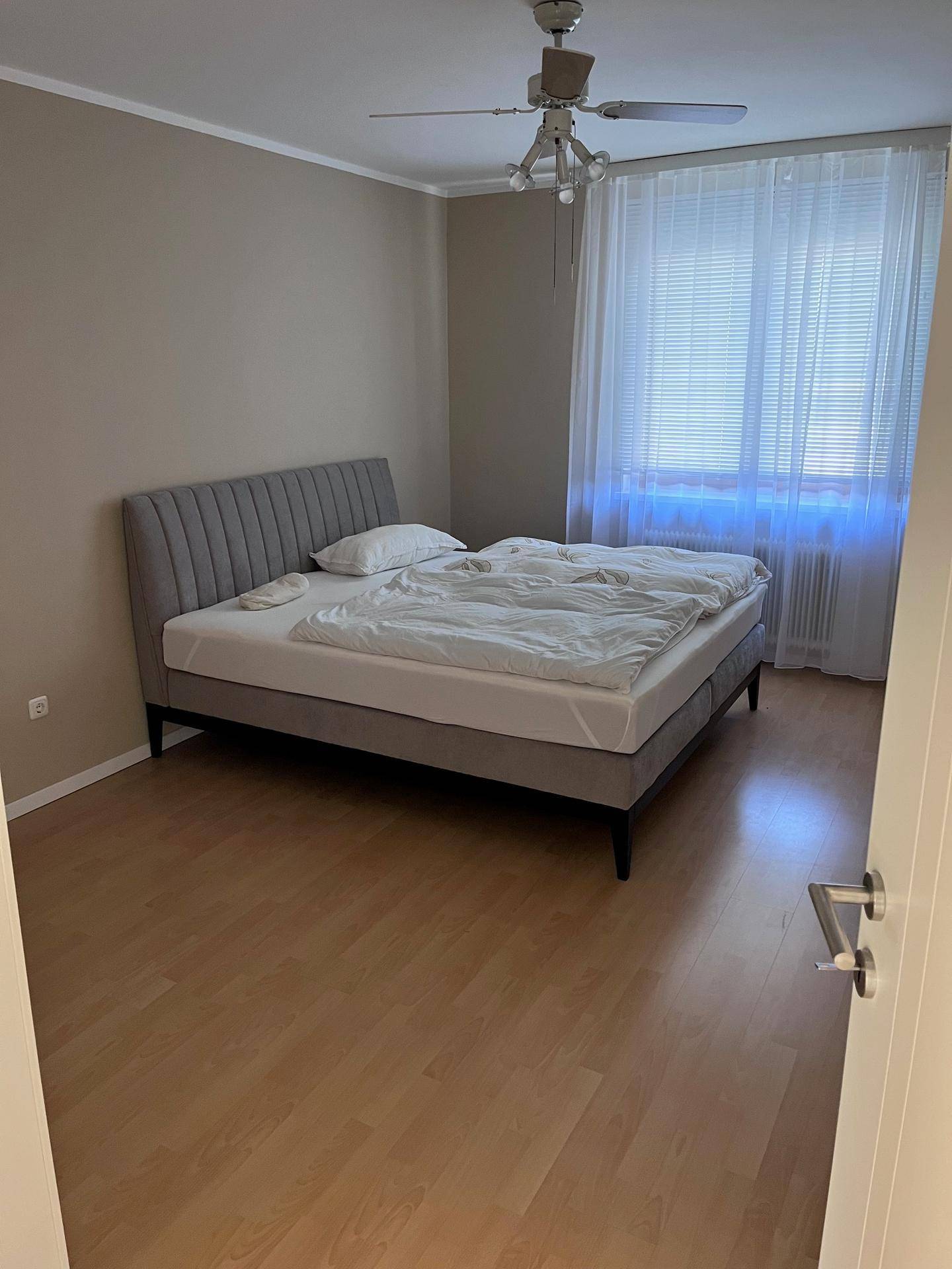 Schlafzimmer mit bequemem Polsterbett, hellem Boden und Deckenventilator für angenehmes Klima.