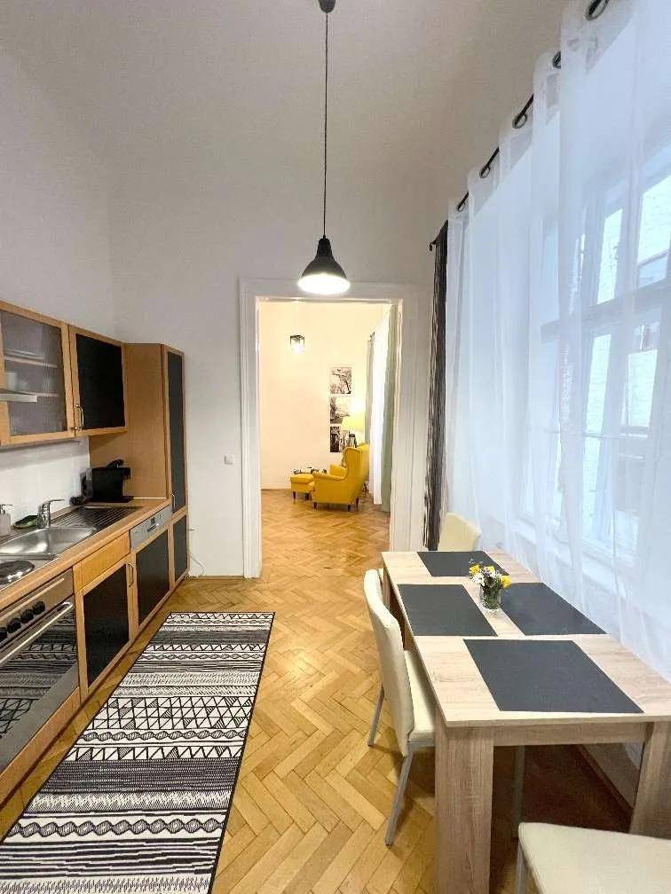 Funktionale Küche mit Essbereich, Holzschränken und Blick in das angrenzende Wohnzimmer durch eine Tür.