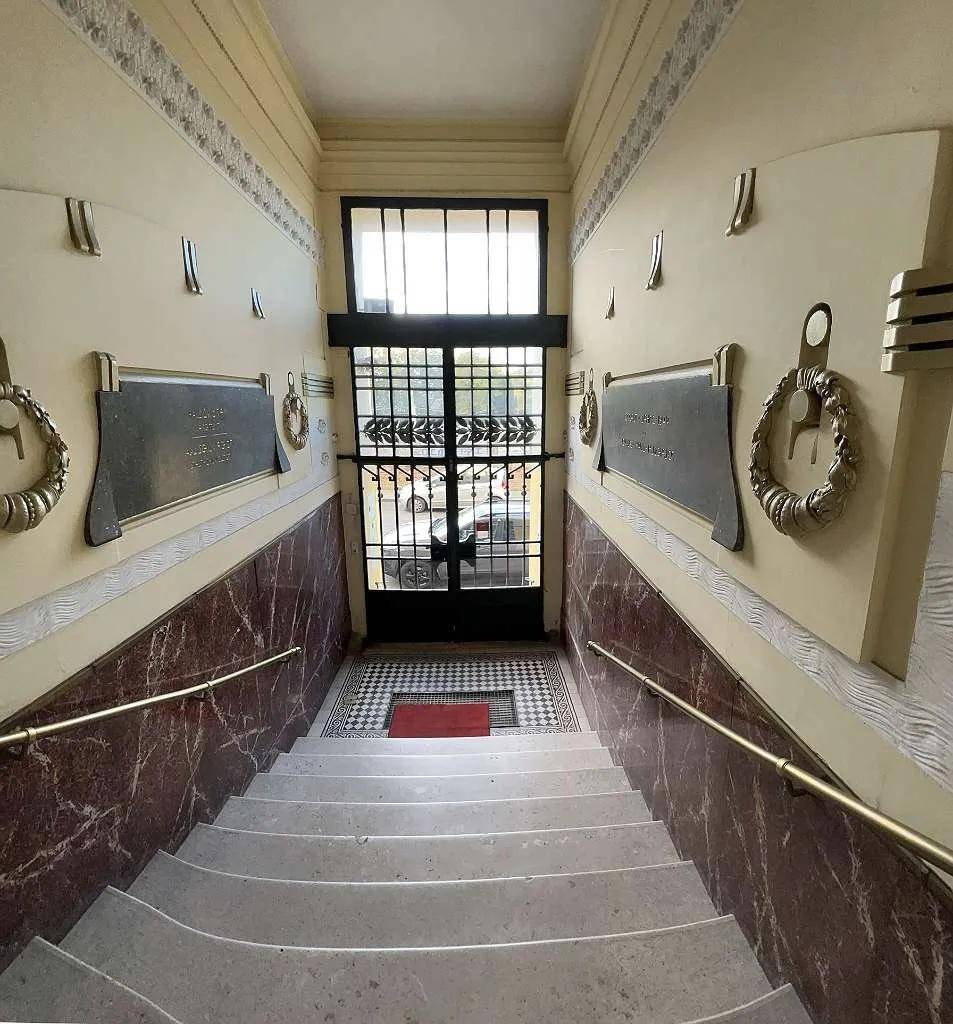 Historisches Treppenhaus mit Marmorverkleidung, dekorativen Elementen und einem schmiedeeisernen Tor am Eingang.