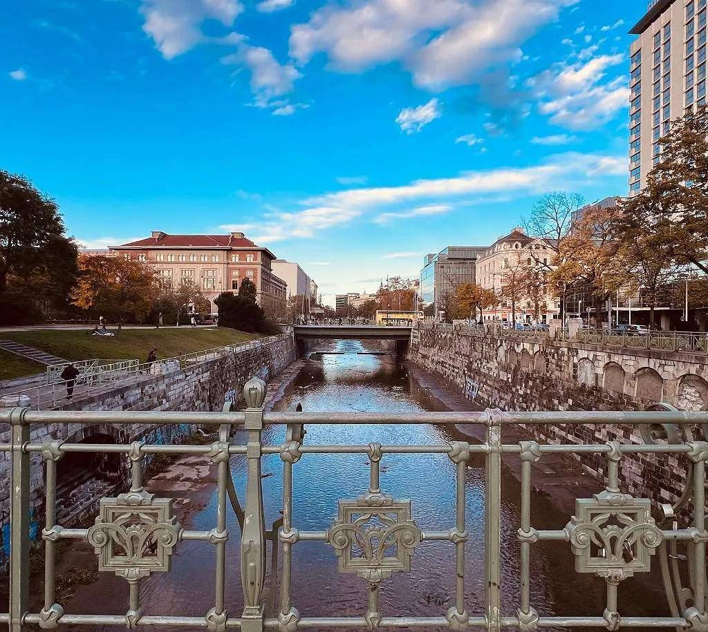 Flussansicht mit Brücke und historischen Gebäuden entlang des Ufers unter einem weiten blauen Himmel.