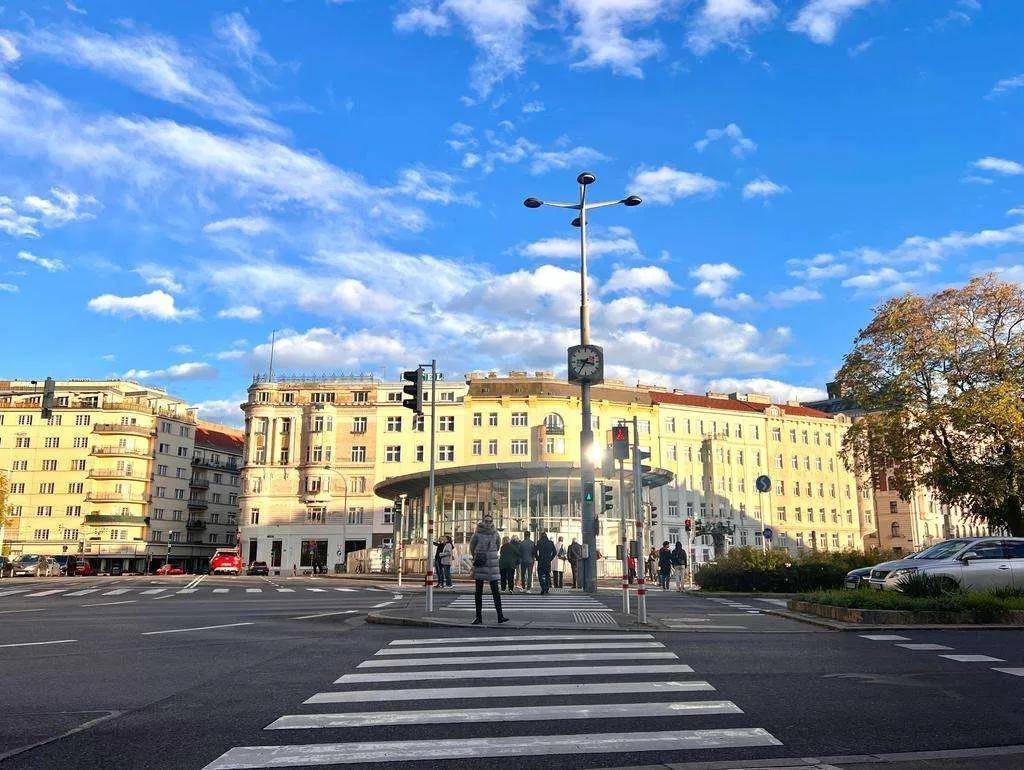 Weitläufige Straßenkreuzung in einer städtischen Umgebung mit historischen Gebäuden unter blauem Himmel.