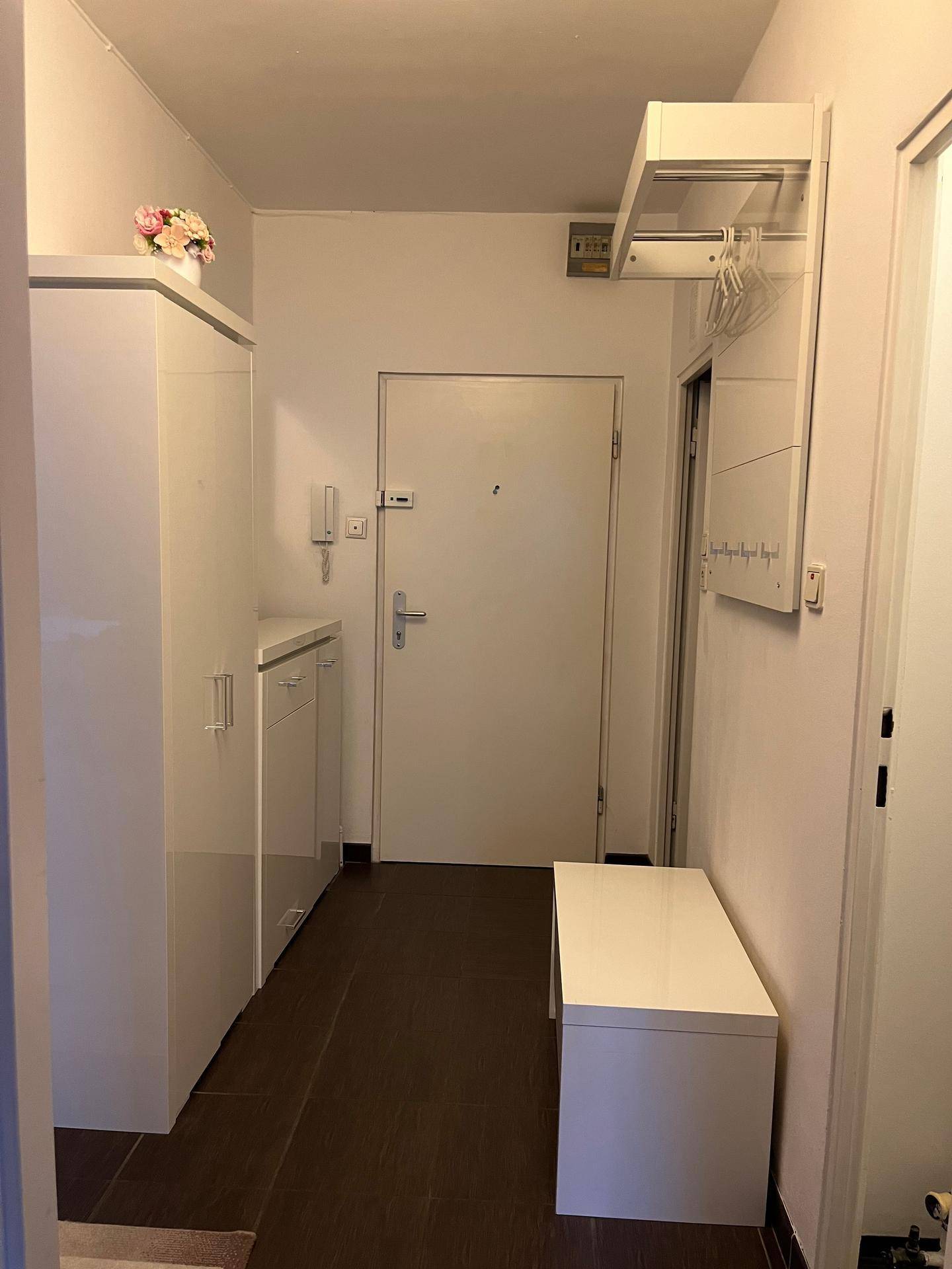 Heller Eingangsbereich mit weißem Schuhschrank, Garderobe und dunklem Fliesenboden.