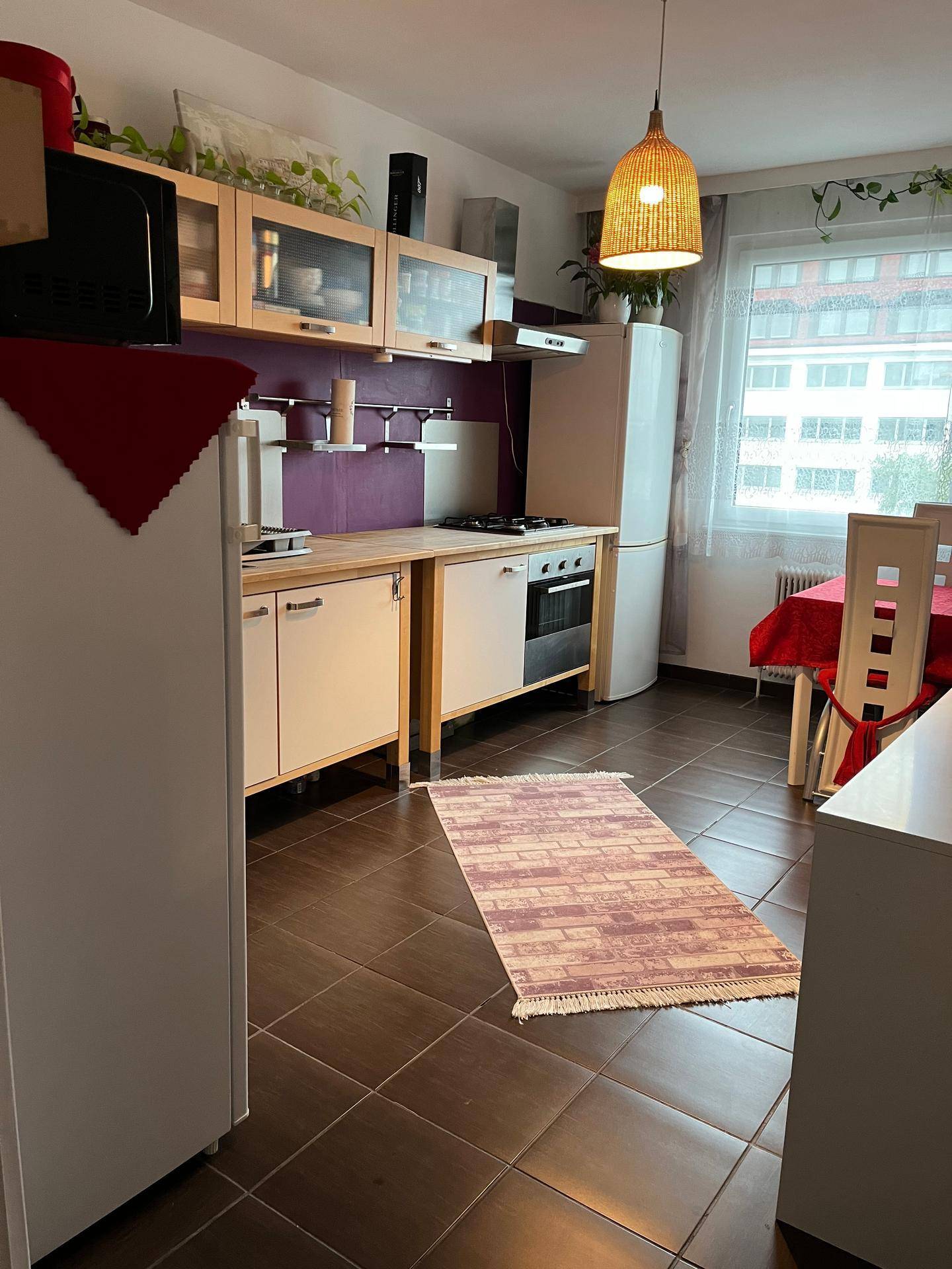 Funktionale Küche mit Holzfronten, lila Akzentwand und Essbereich, ausgestattet mit grundlegenden Geräten.