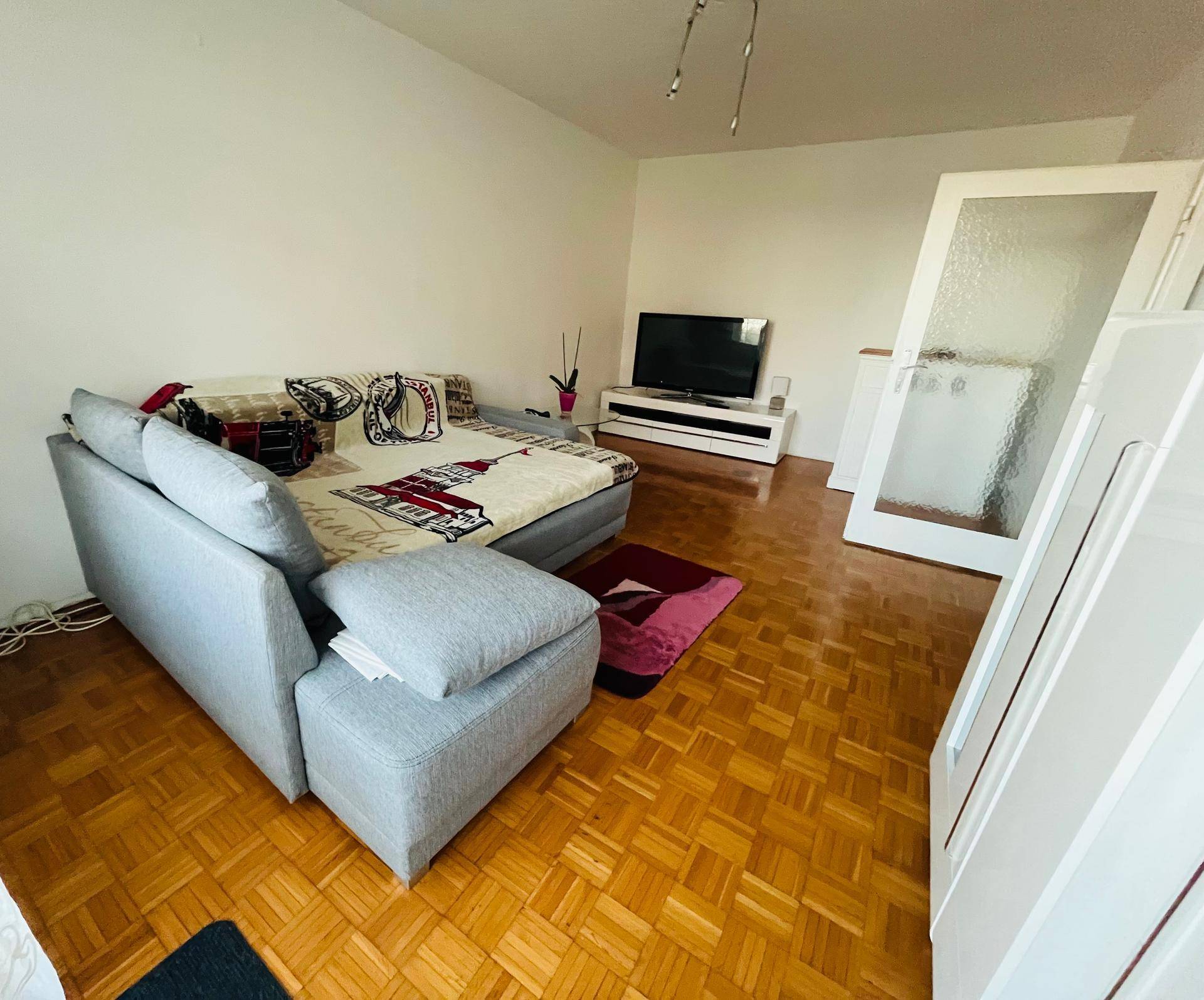 Geräumiges Wohnzimmer mit Parkettboden, großem Sofa und Fernseher, ideal für entspannte Abende.