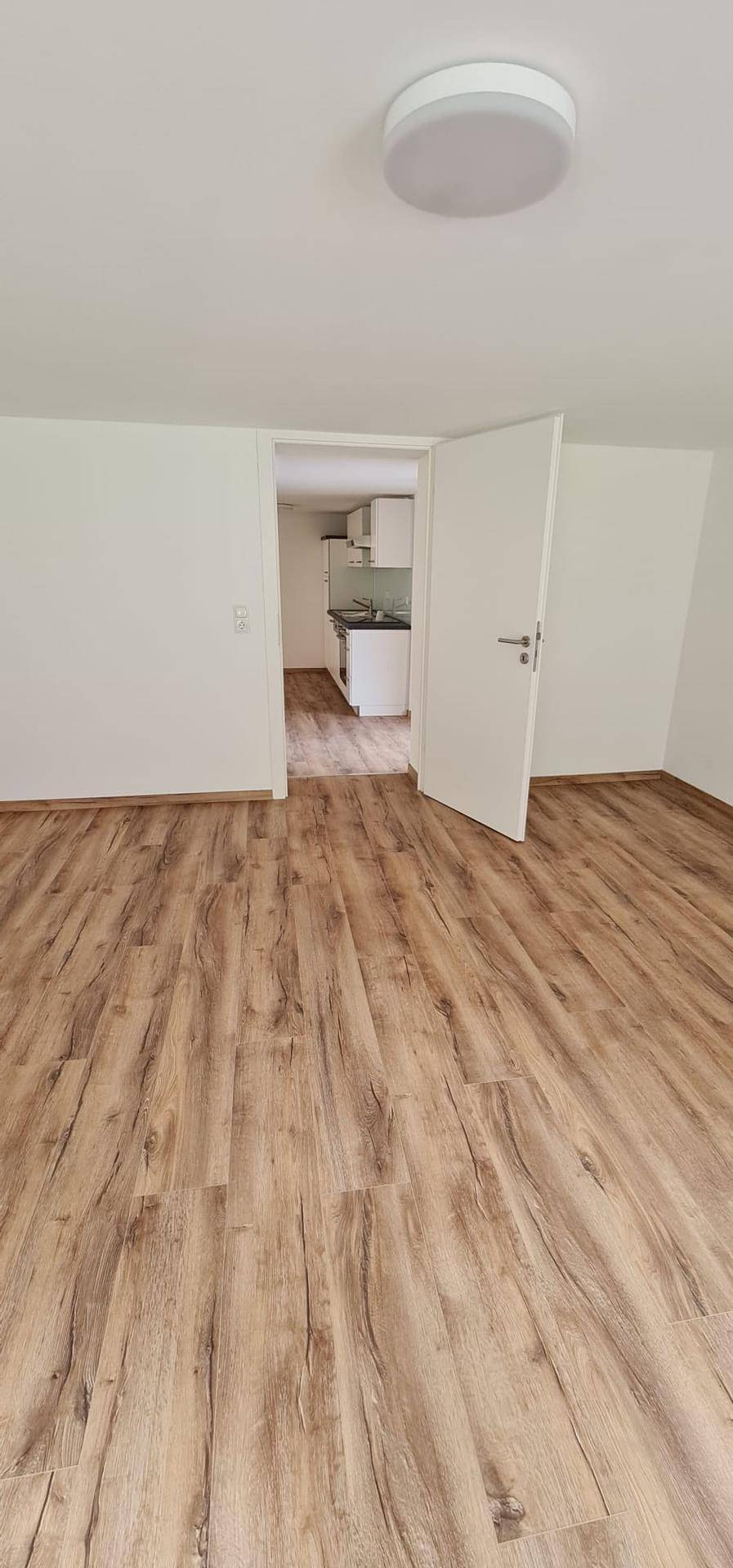 Heller Raum mit Holzboden und Zugang zu einer separaten, funktionalen Küchenzeile.