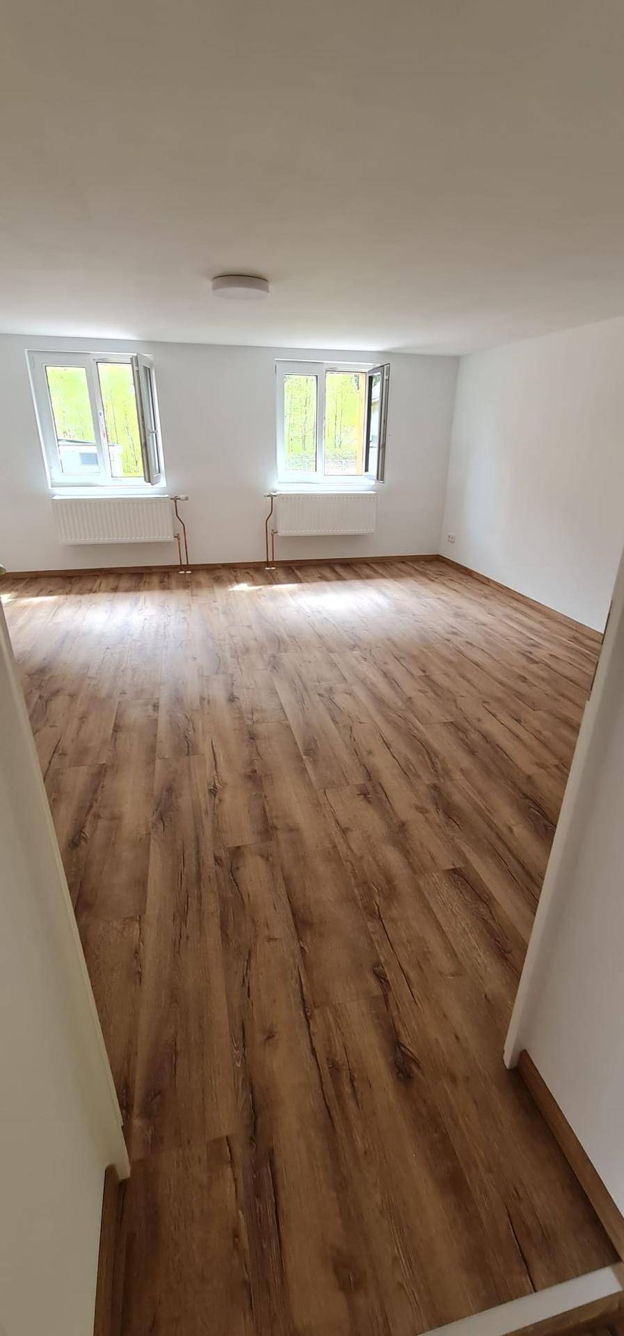 Helles Zimmer mit zwei Fenstern, die für gute Belichtung sorgen, und einem warmen Holzboden.