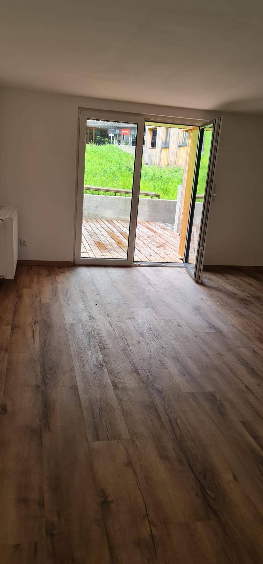 Große Glasschiebetür bietet Zugang zu einer Holzterrasse und lässt viel Licht in den Wohnbereich.