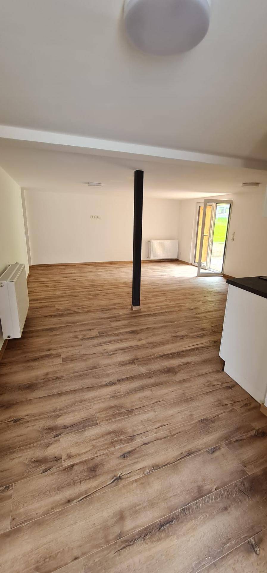 Geräumiger Wohnbereich mit Holzboden, einer zentralen Säule und direktem Zugang zur Außenterrasse.