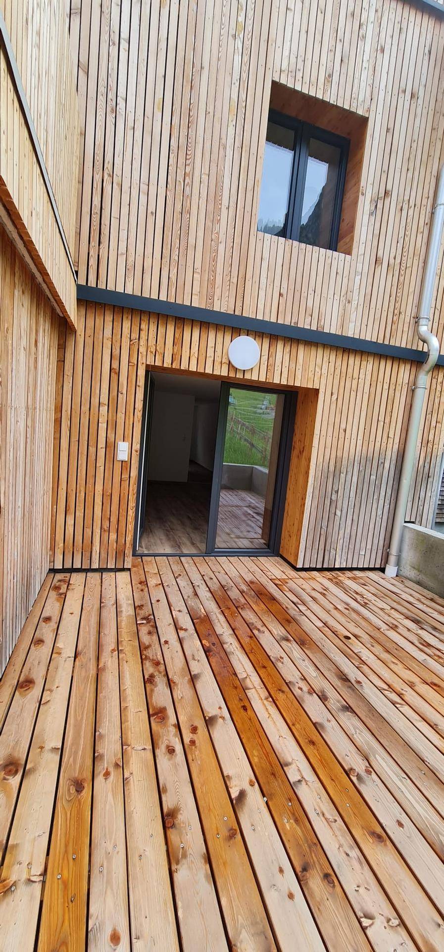 Geräumige Holzterrasse vor einer modernen Fassade mit Holzverkleidung und Blick ins Grüne.