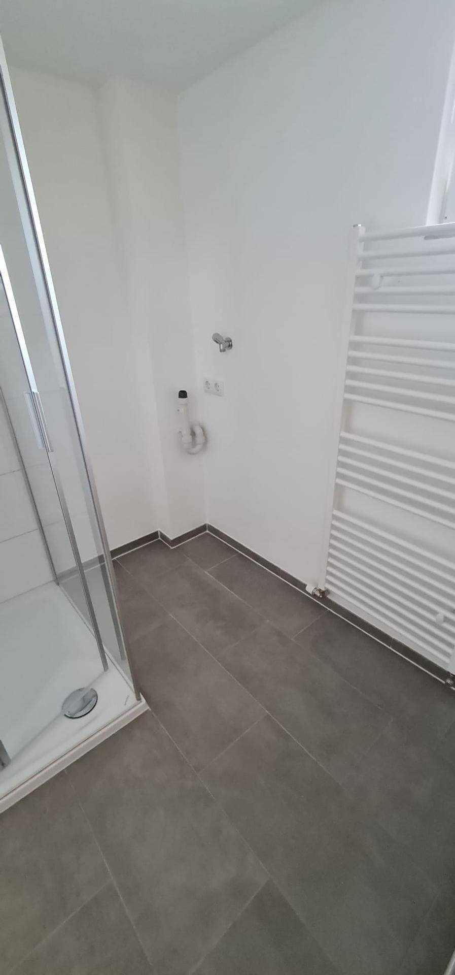 Modernes Badezimmer mit grauen Fliesen, einer Glasdusche und einem praktischen Handtuchheizkörper.