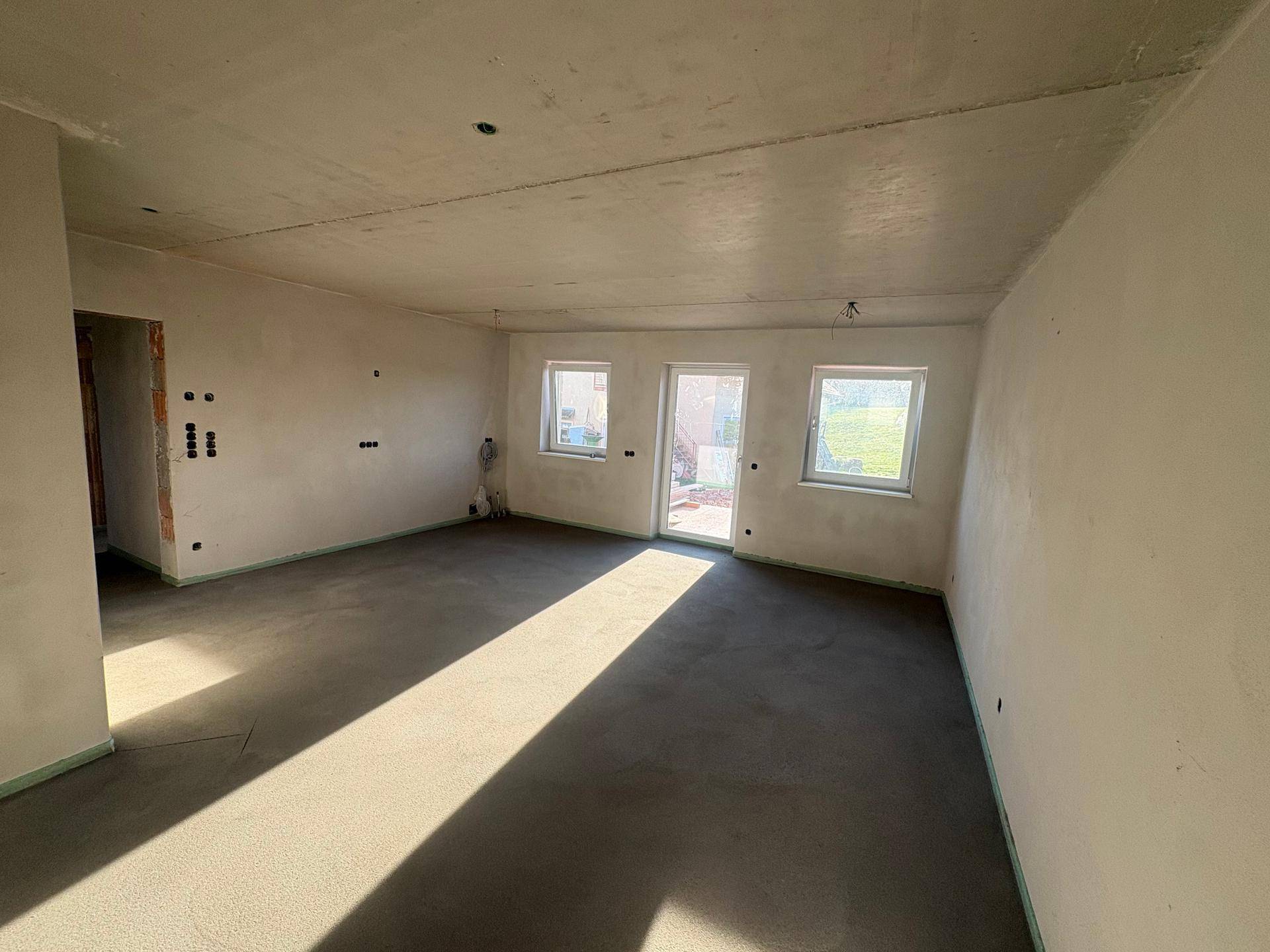 Heller, unmöblierter Wohnbereich im Neubau mit viel Tageslicht durch drei Fenster und Türen.