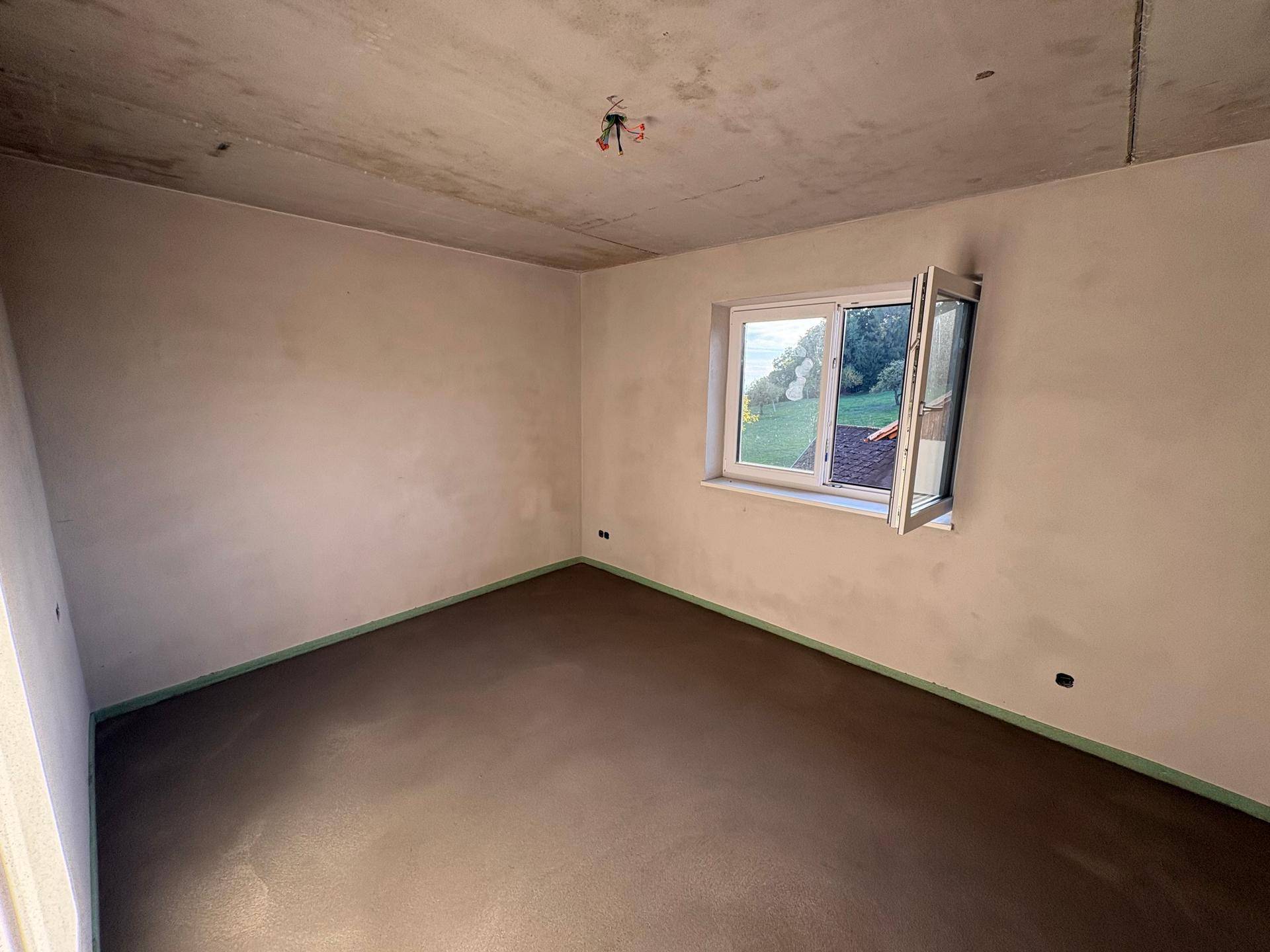 Unmöblierter Raum im Neubau mit einem geöffneten Fenster, das viel Tageslicht und Grünblick bietet.