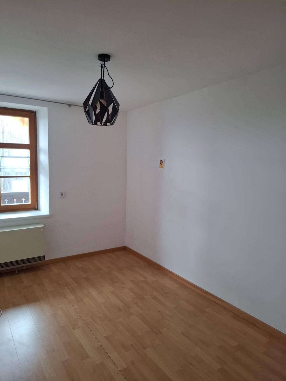 Helles Zimmer mit Laminatboden, einem Fenster und einer modernen Deckenleuchte.