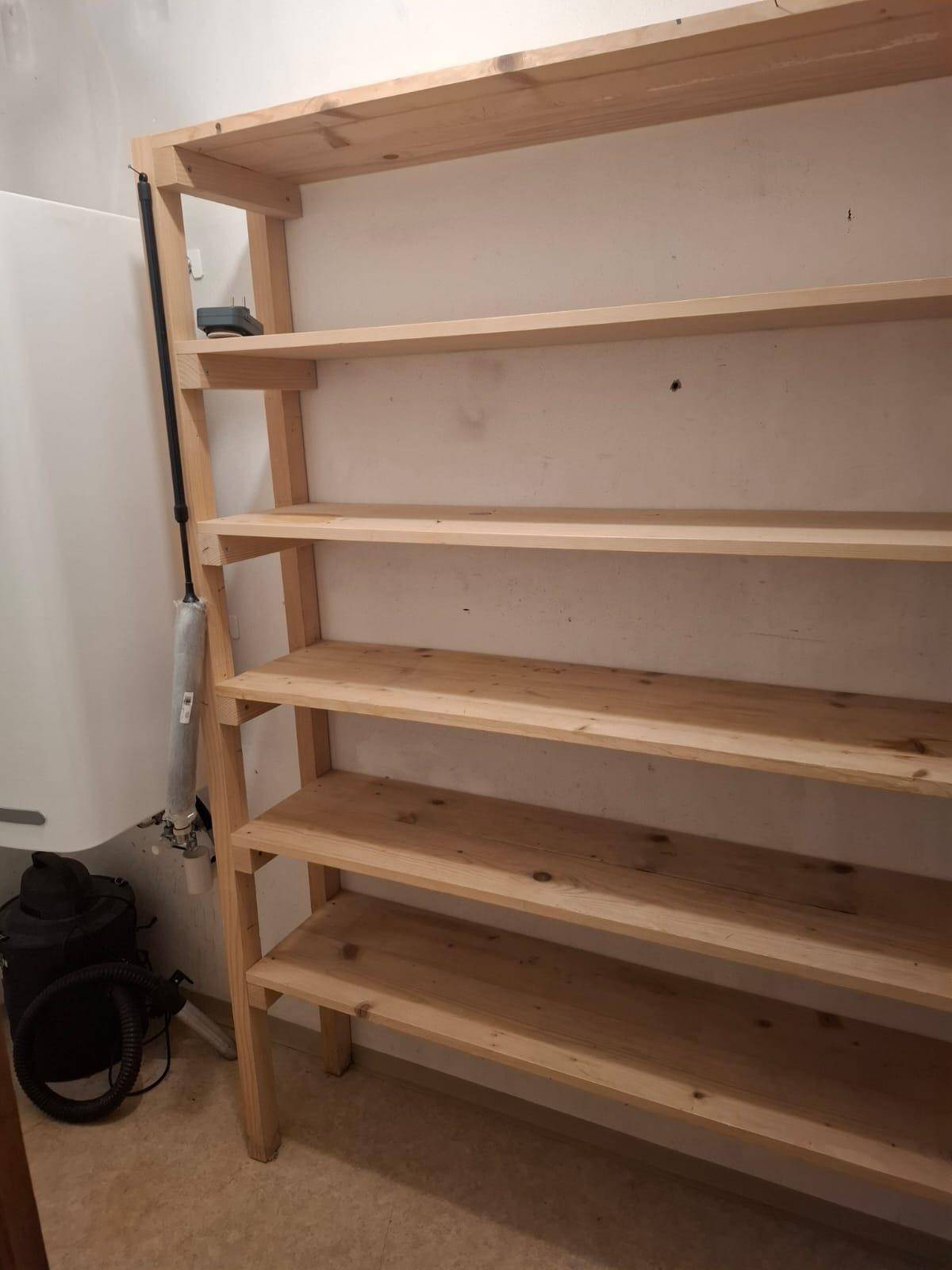 Praktischer Abstellraum mit einfachen Holzregalen und einem Warmwasserbereiter an der Wand.