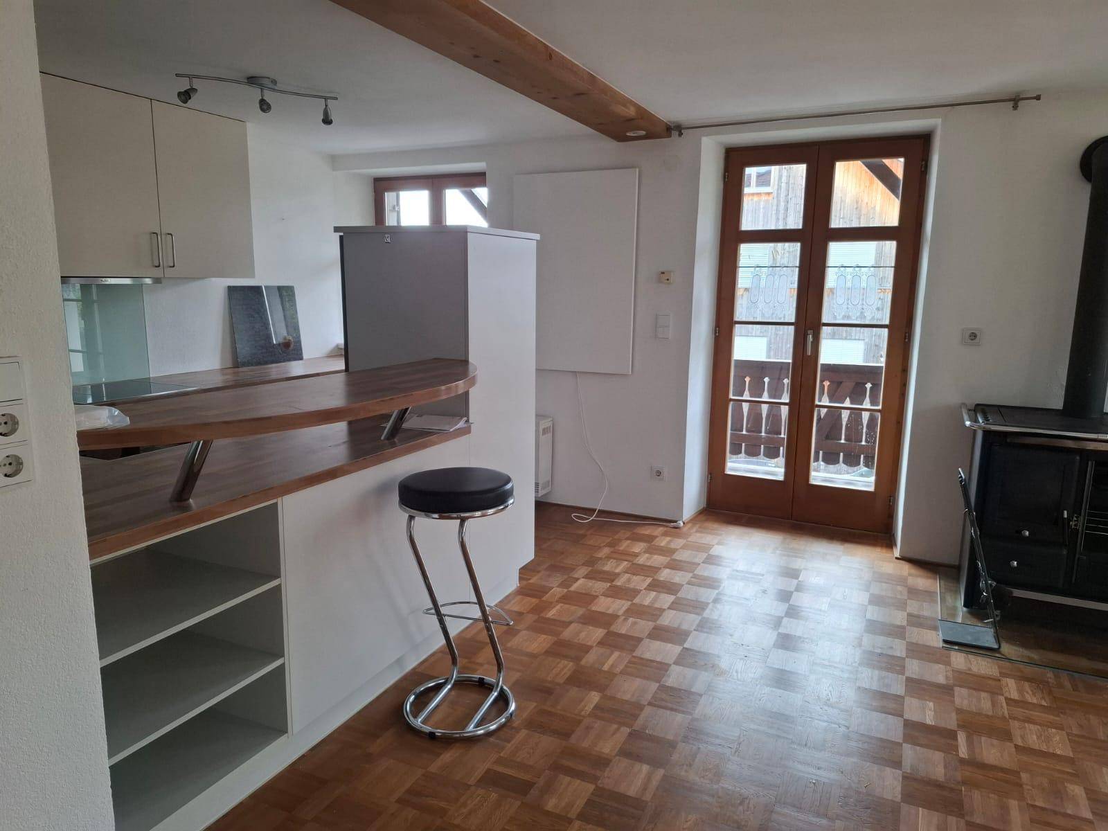 Offener Wohnbereich mit integrierter Küche, Frühstücksbar, Holzbalken und Balkonzugang.