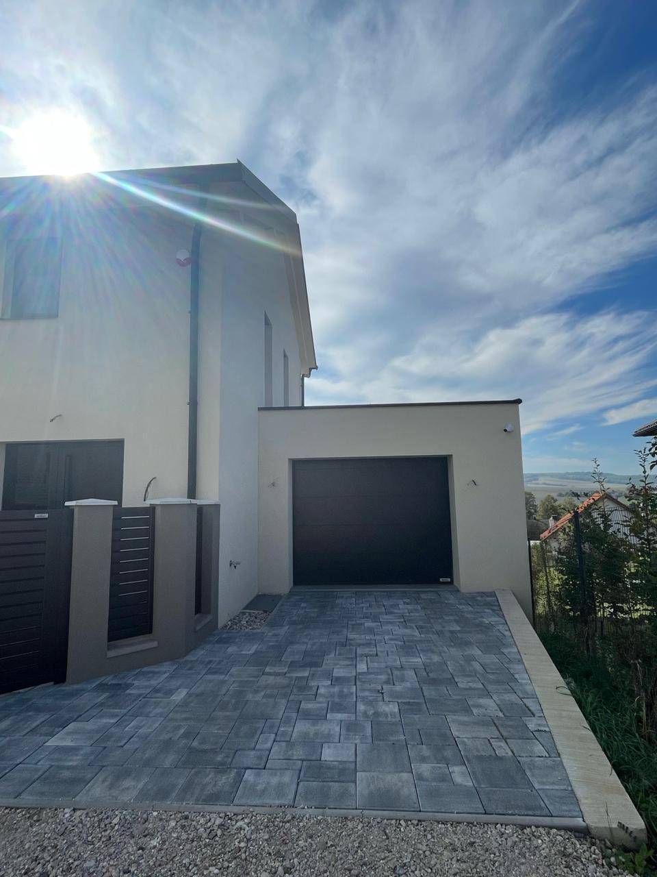 Modernes Einfamilienhaus mit integrierter Garage und gepflasterter Zufahrt unter blauem Himmel.