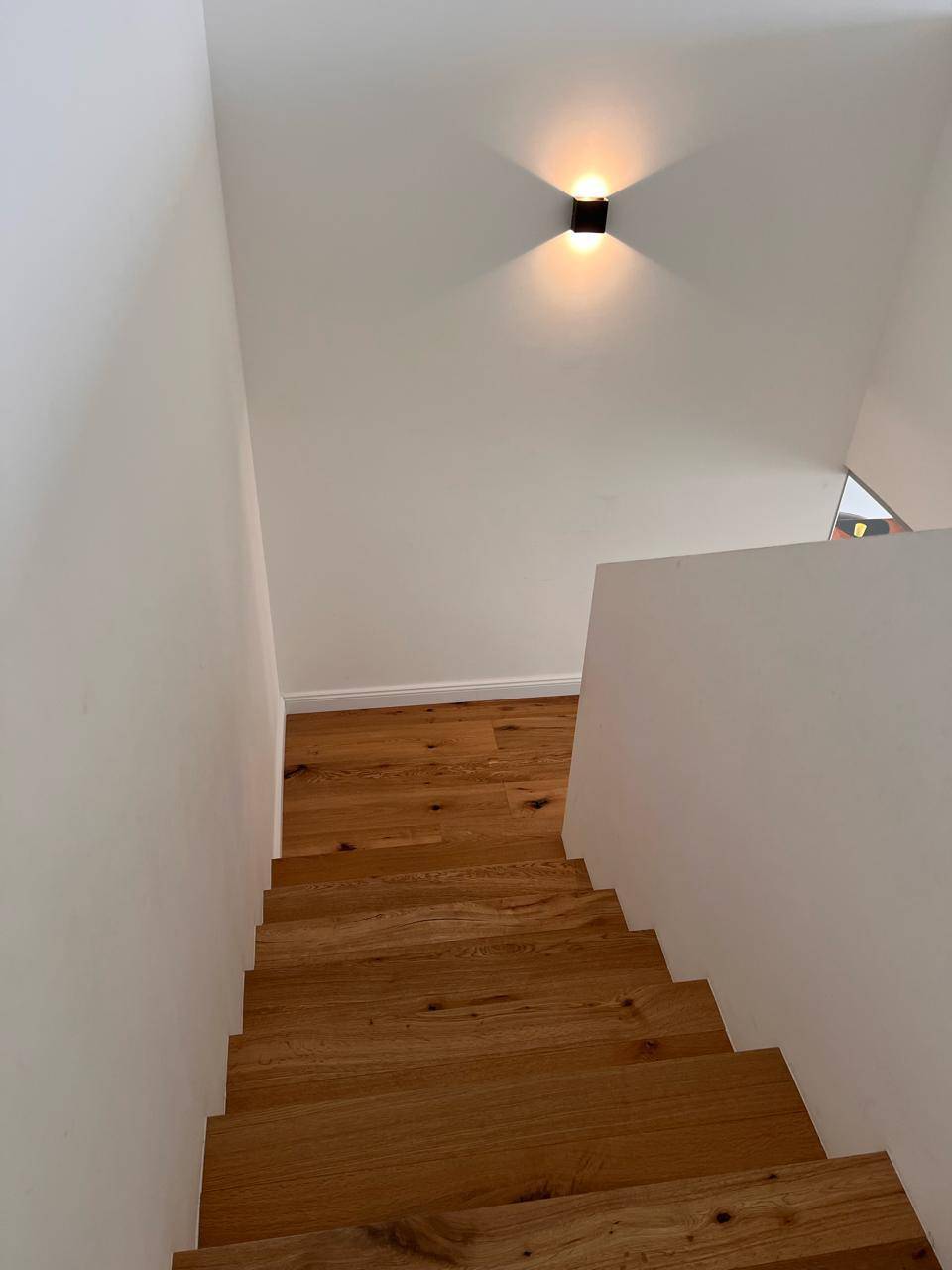 Heller Treppenaufgang mit Holzstufen und minimalistischer Wandbeleuchtung.