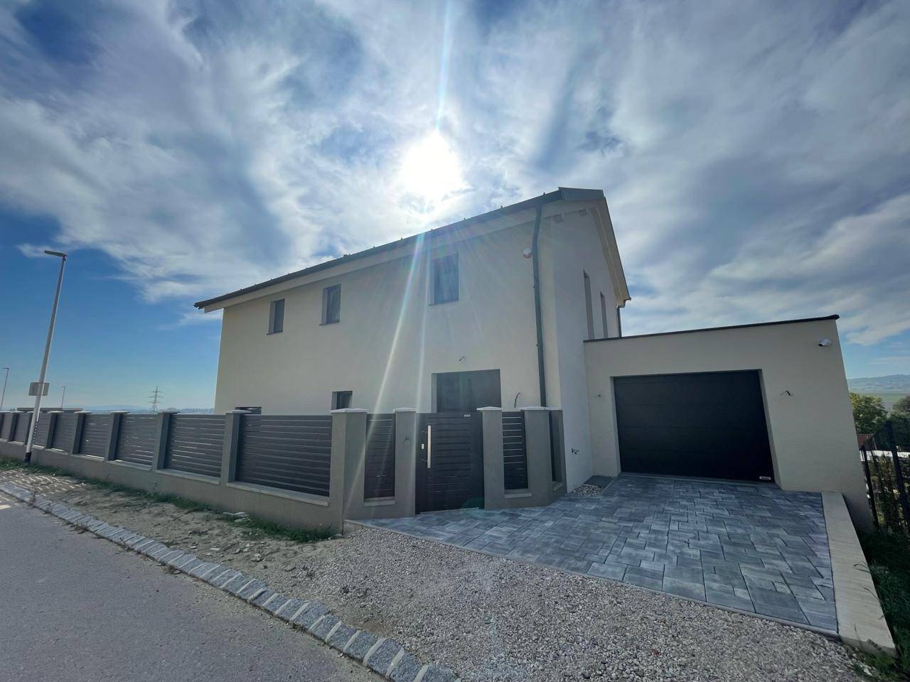 Neubau-Einfamilienhaus mit moderner Fassade, Garage und gepflegter Außenanlage an sonnigem Tag.