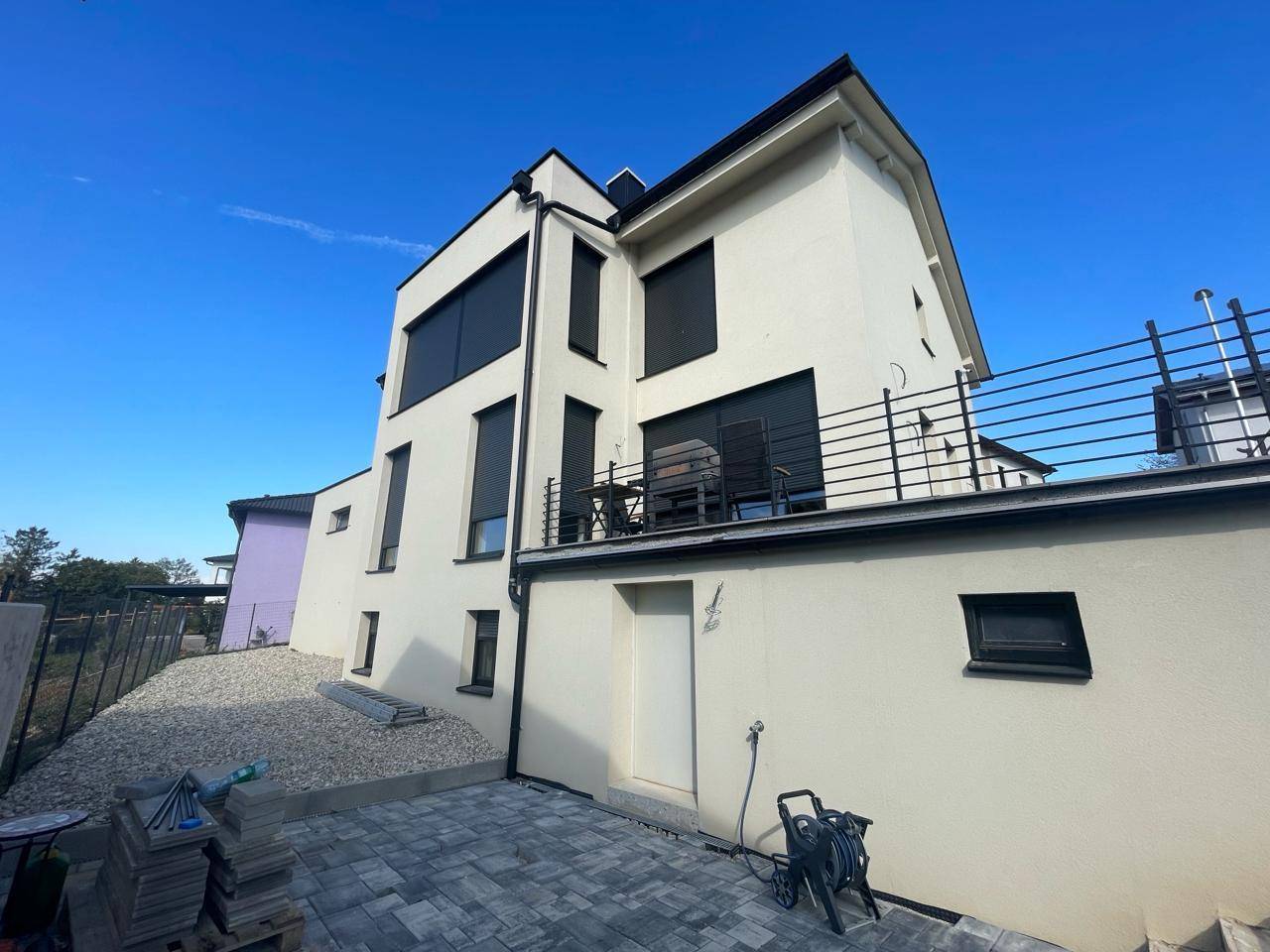 Rückansicht des modernen Hauses mit Terrasse, gepflastertem Bereich und Blick in die Umgebung.