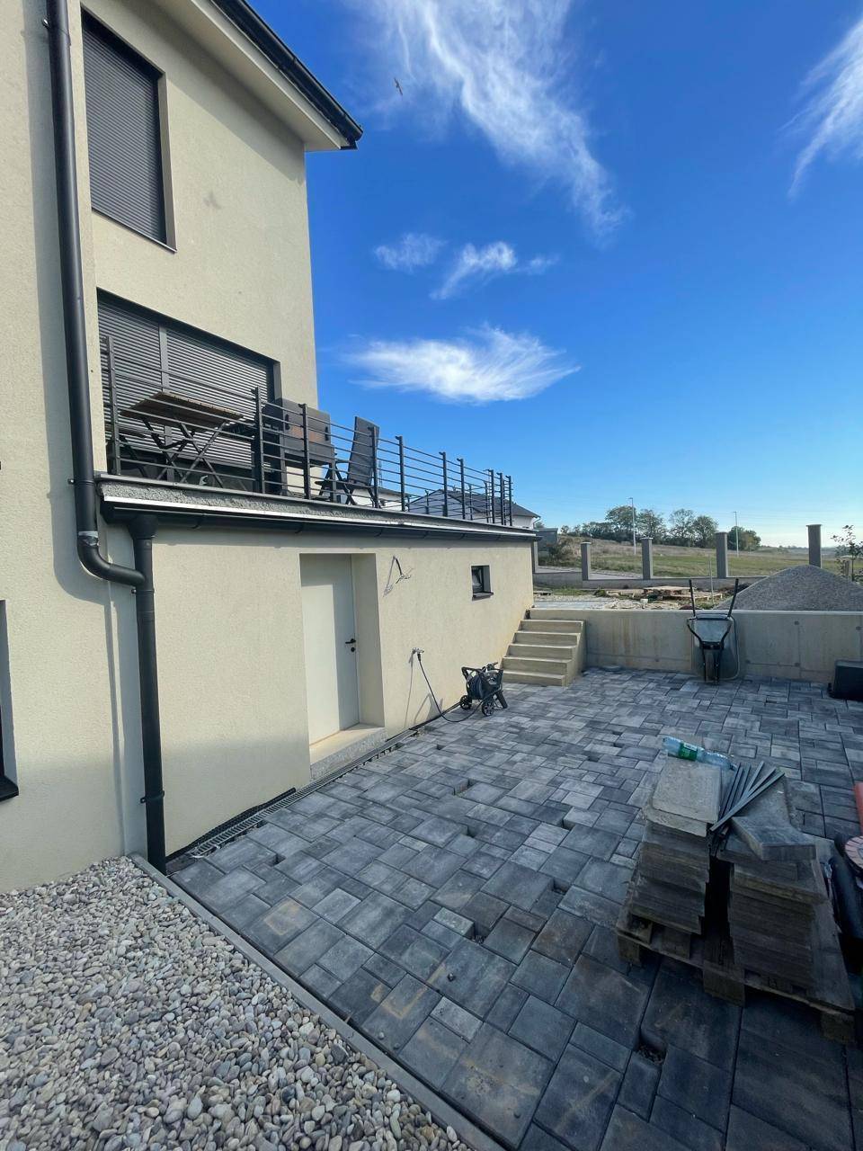 Gepflasterter Außenbereich mit Treppe zur oberen Terrasse und Zugang zum Haus.