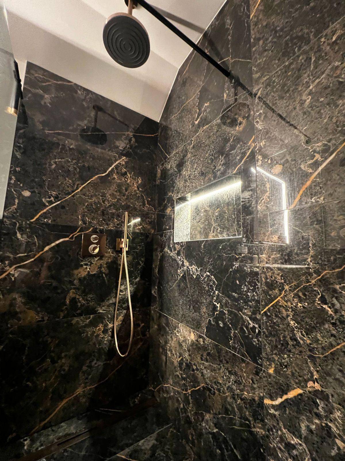 Detailansicht der begehbaren Dusche mit dunklen Marmorfliesen und goldfarbenen Armaturen.