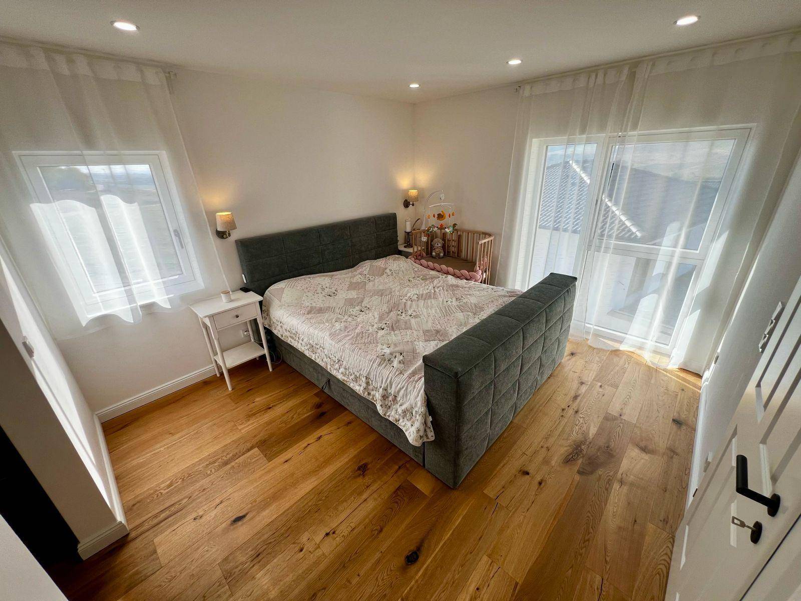 Helles Schlafzimmer mit Holzboden, Doppelbett und Zugang zum Balkon.
