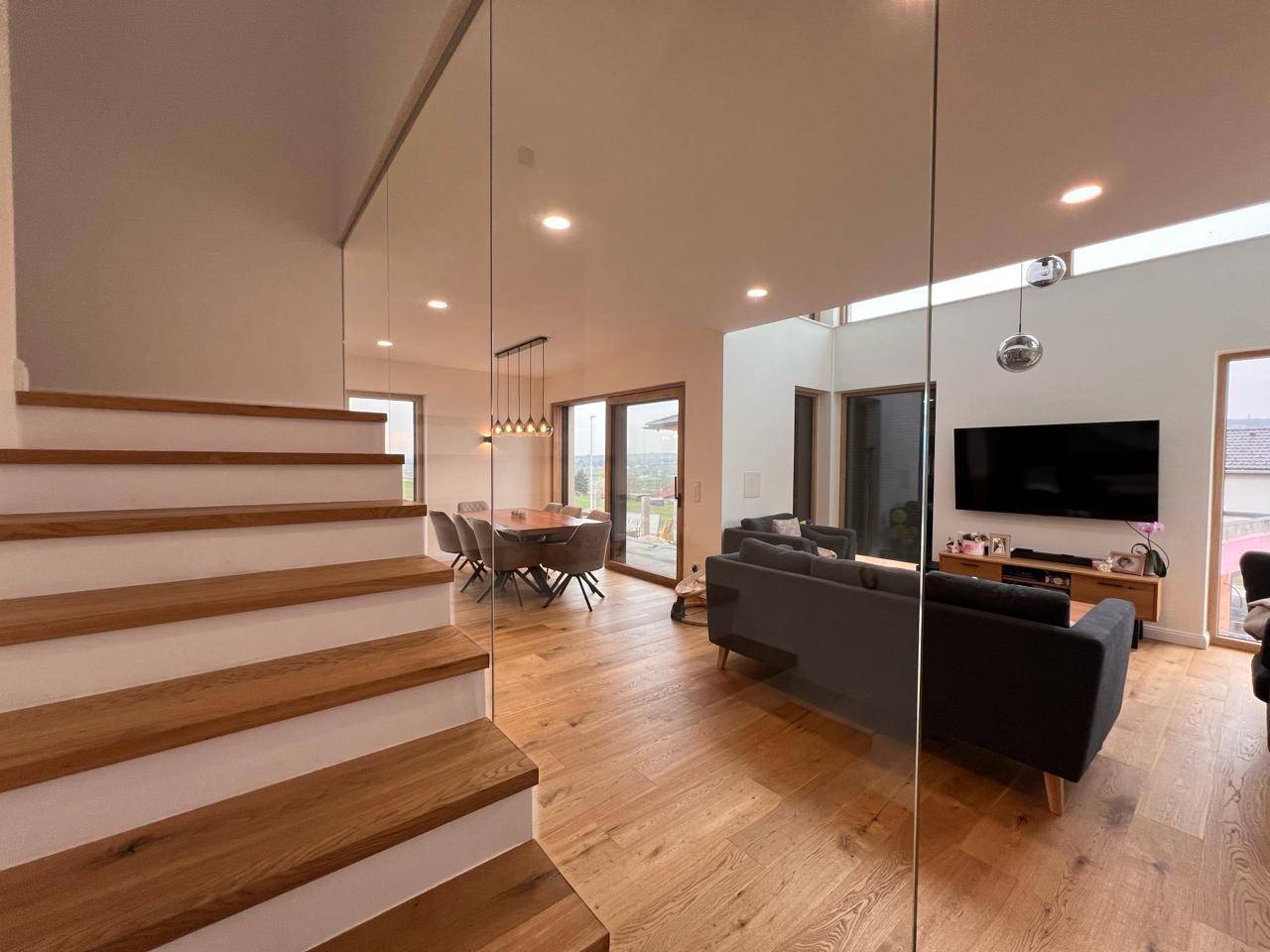 Offener Wohn-Essbereich mit Holzboden, moderner Treppe und Zugang zur Terrasse.