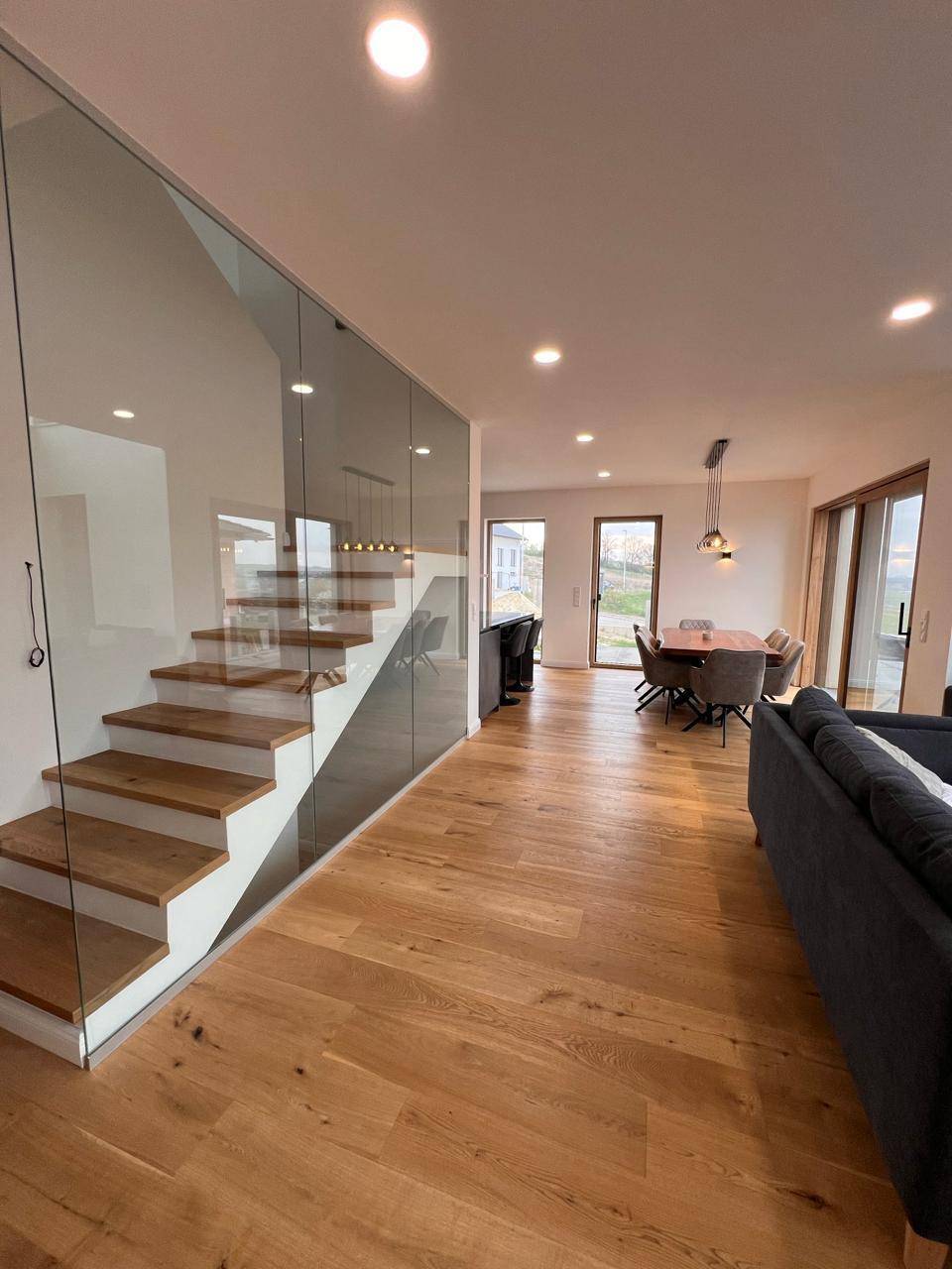Heller Wohnbereich mit eleganter Holztreppe und Glasgeländer, offen zum Essbereich.